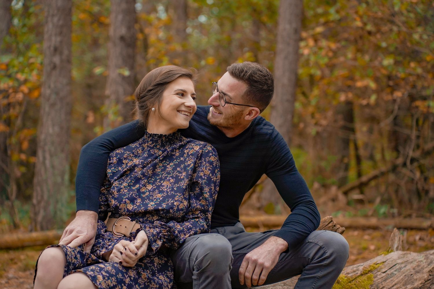 A romantic couple shares tender moments in a fall forest setting with golden autumn leaves.