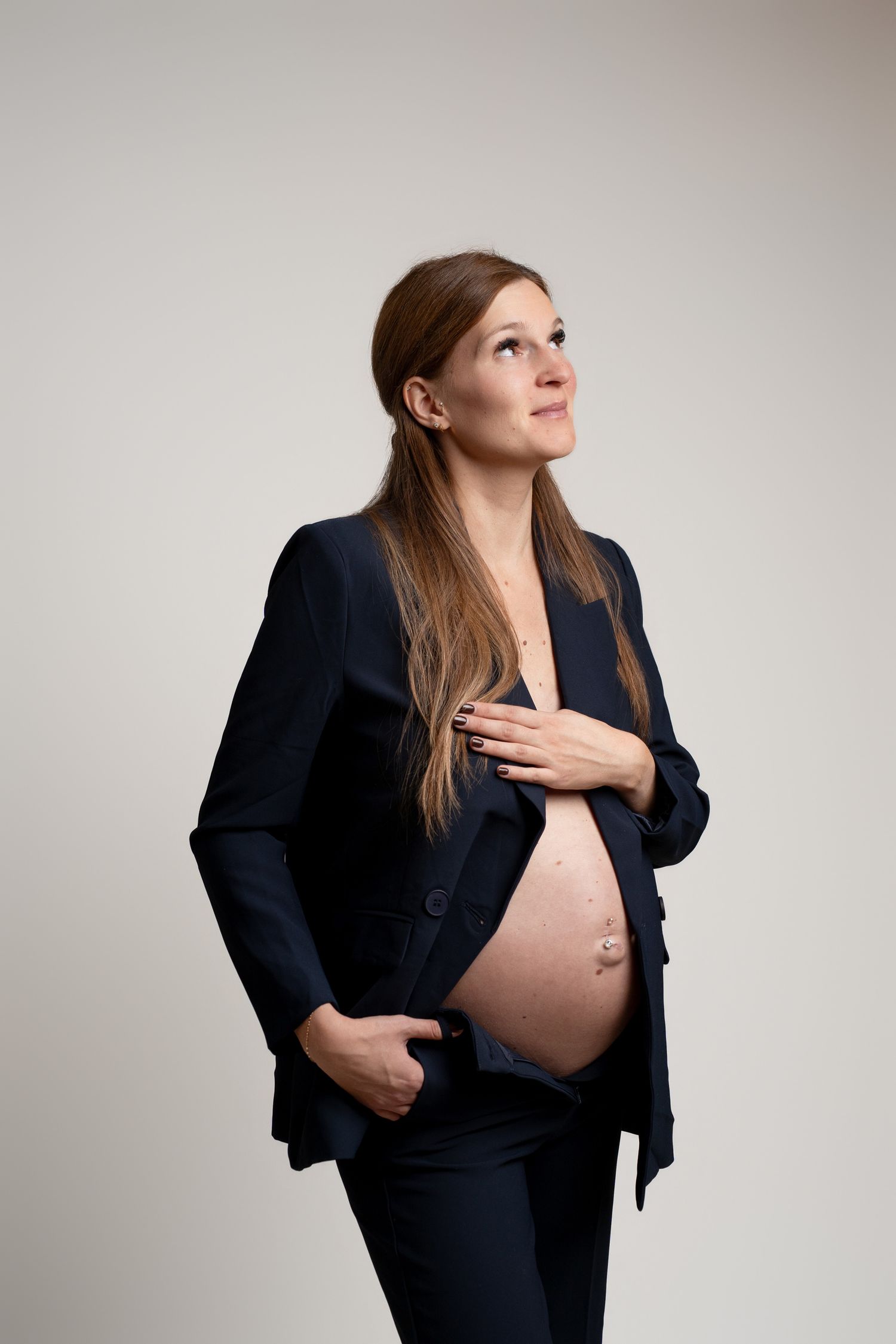 Professional maternity portraits in business attire against neutral backdrop.