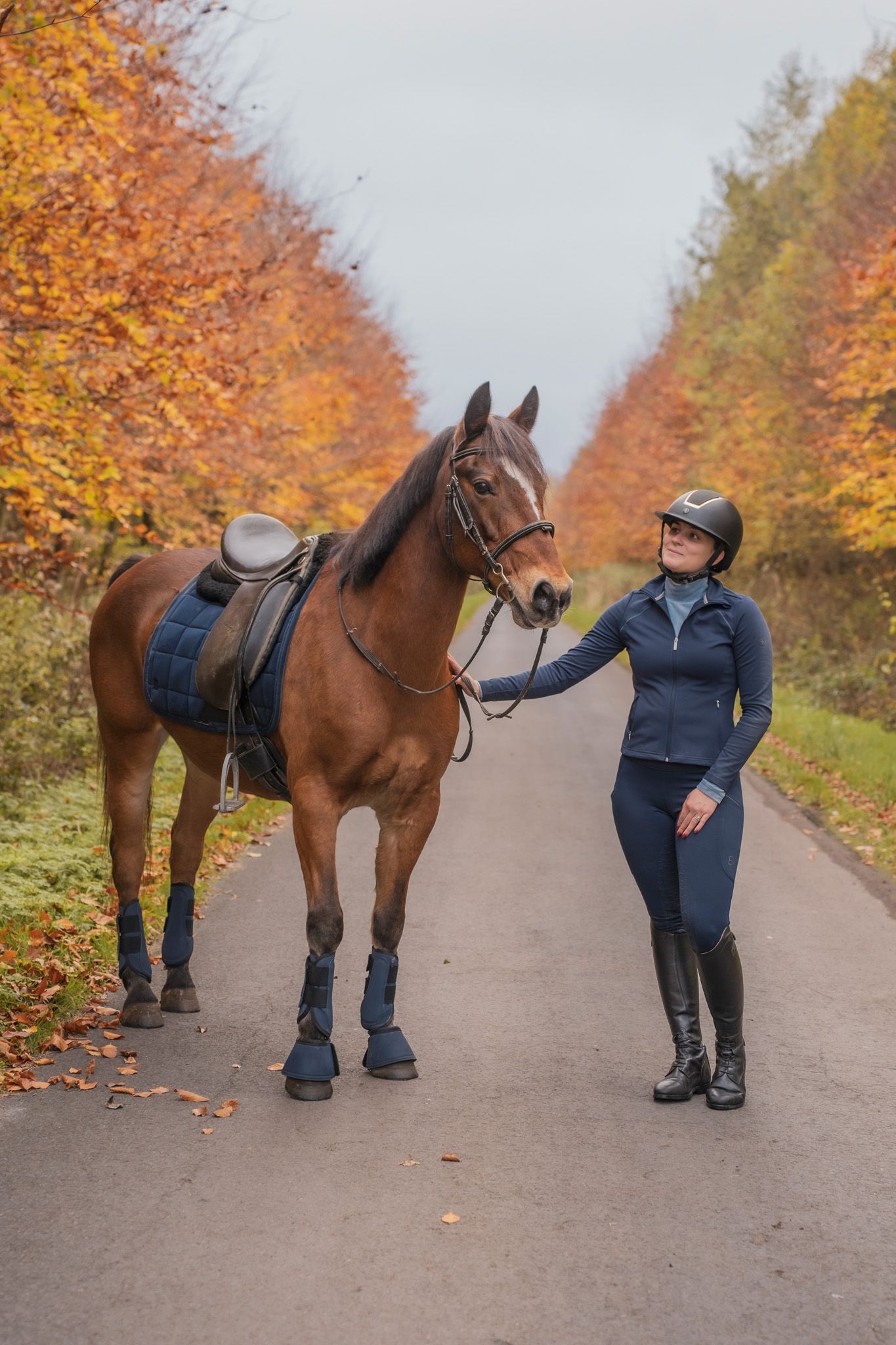 Horse and rider performing stretching exercises on a tree-lined path with orange autumn leaves.