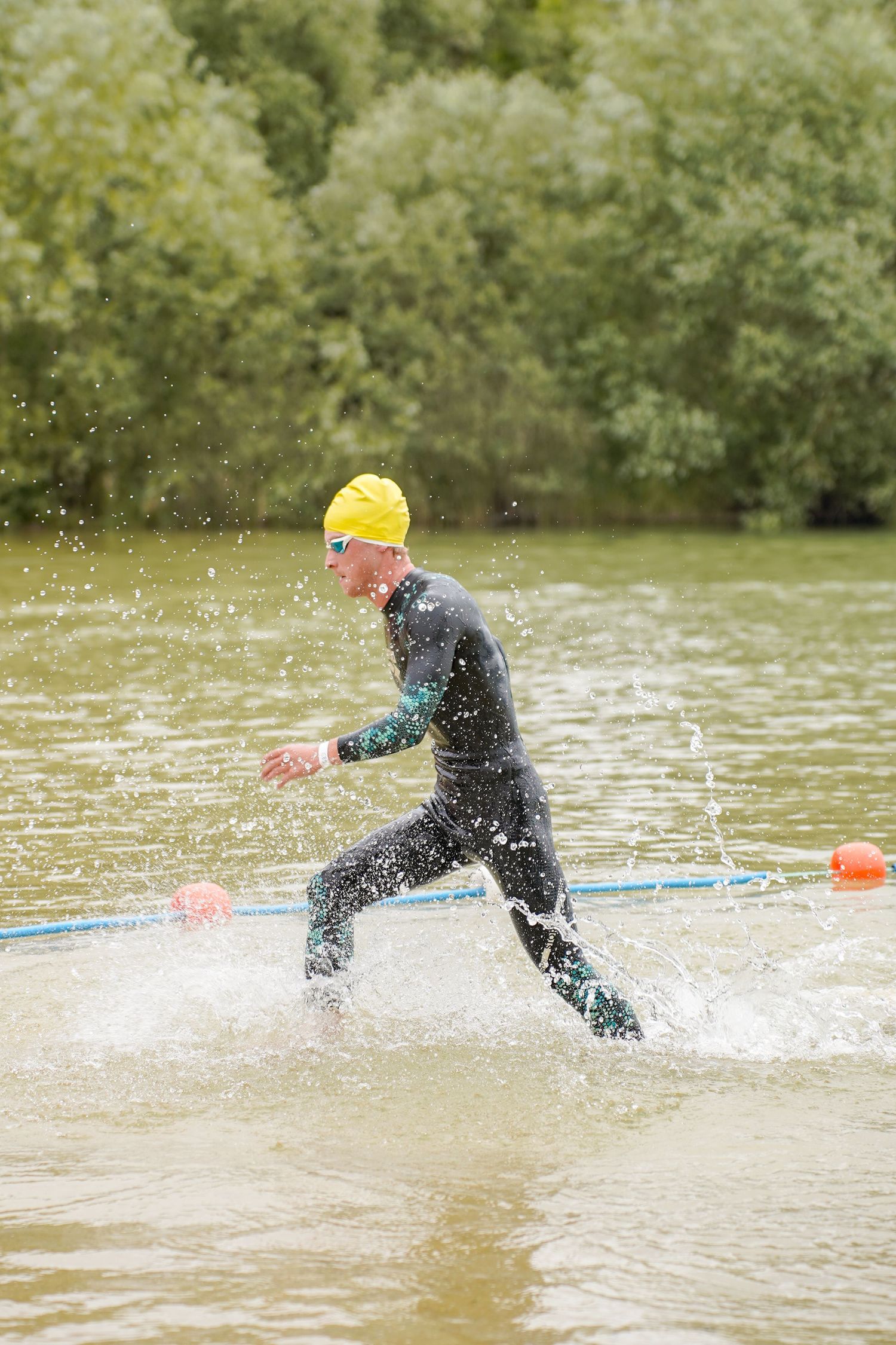 Swimmers in wetsuits splashing through water during triathlon race.