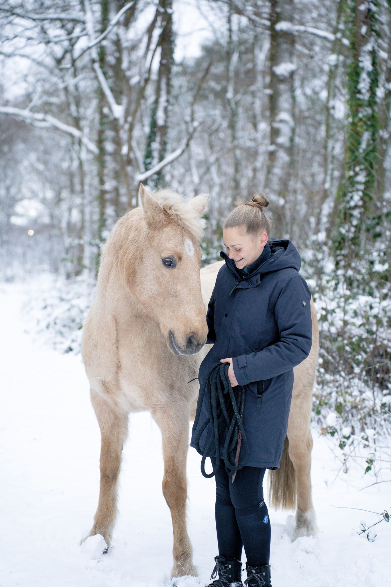 A palomino horse and companion share a winter moment in a snow-covered forest landscape.