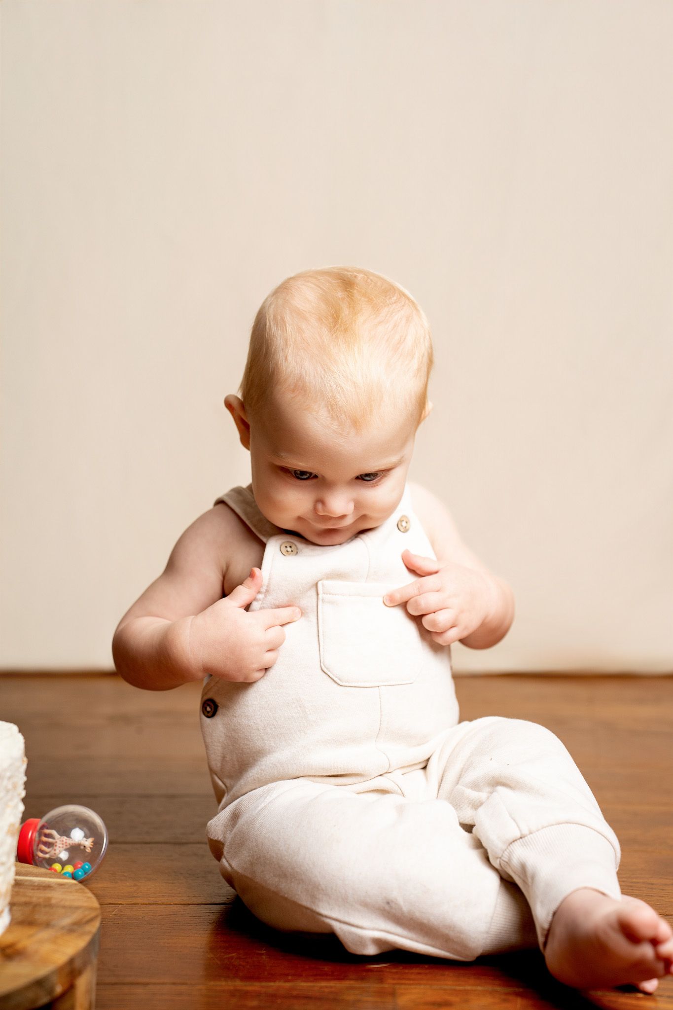 Baby in cream overalls explores during indoor photo session.