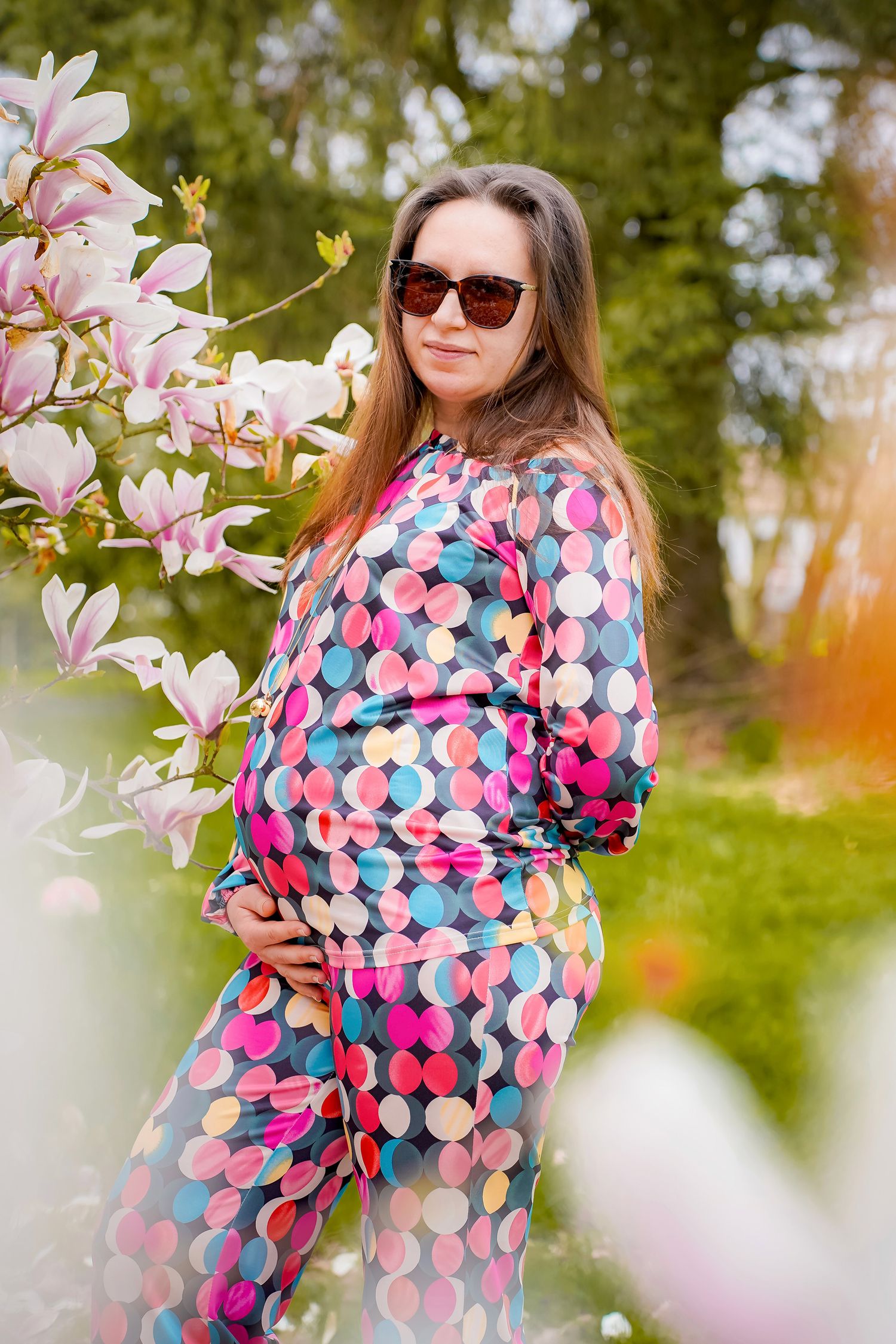 Maternity portraits amid blooming magnolia trees wearing a colorful polka dot dress.