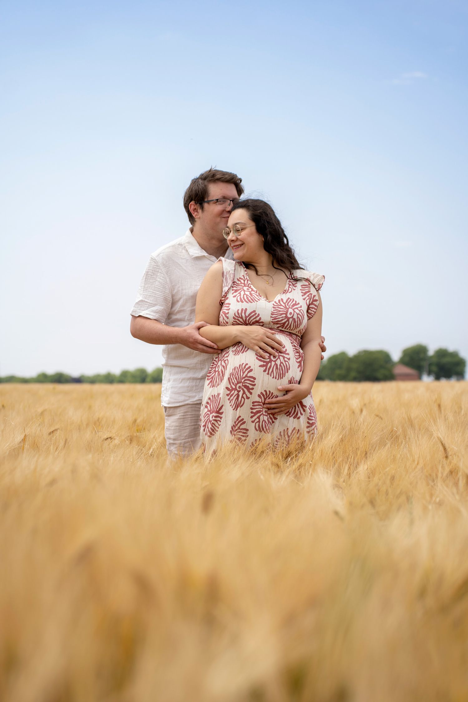 A romantic couple embraces in a golden wheat field on a sunny summer day.