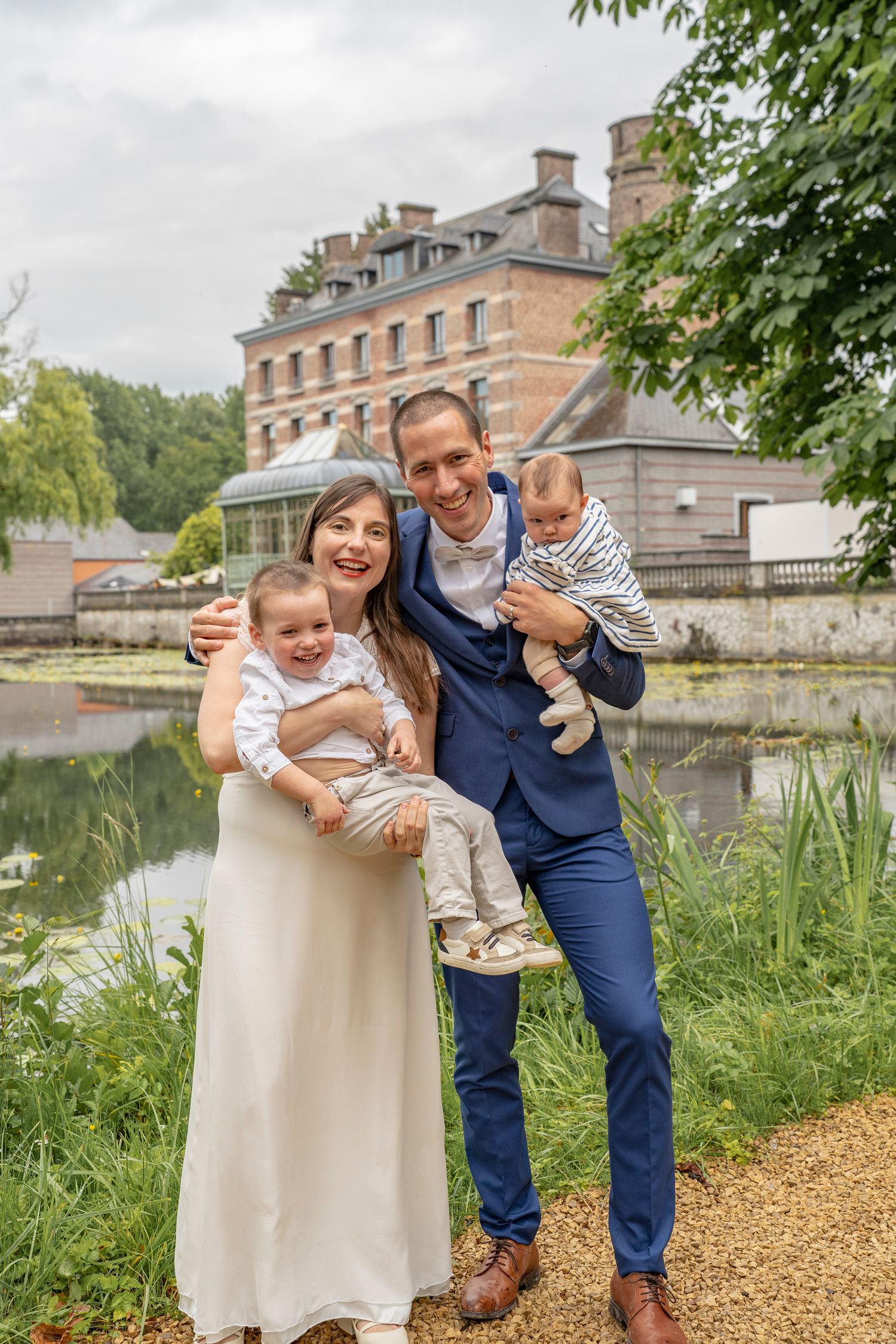 Family shares playful moment together by lakeside with historic building in background.