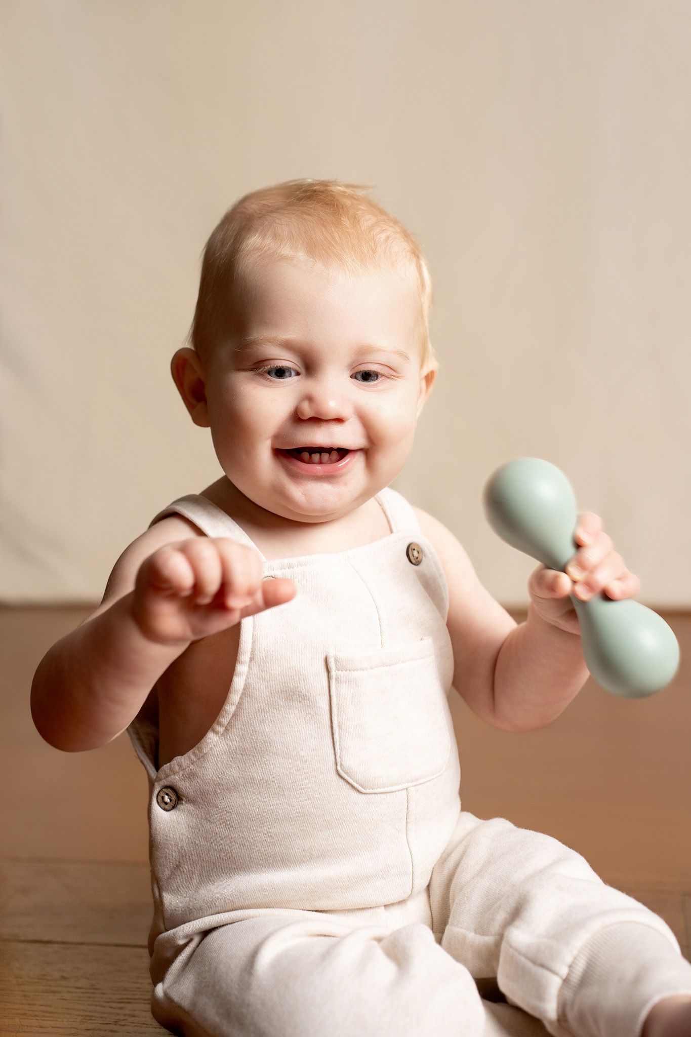 Baby in white outfit plays with blue toy during studio photo session.