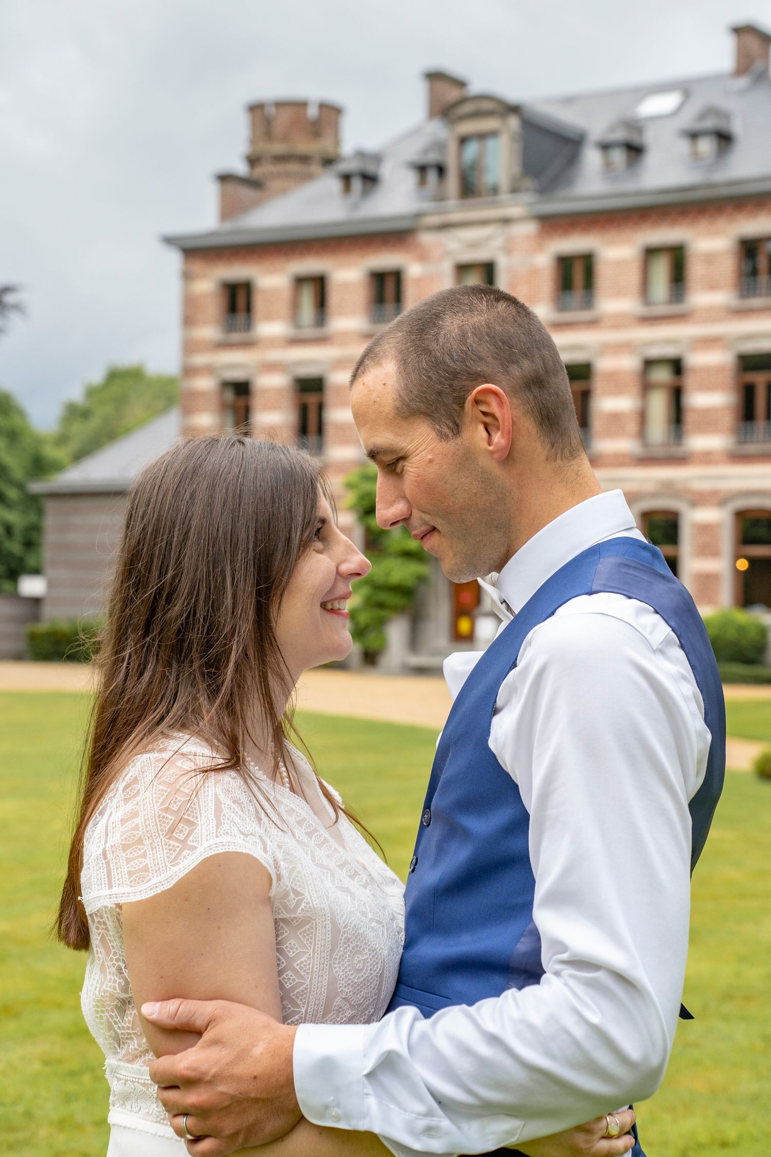 A couple shares a tender moment on the lawn of a grand brick estate.