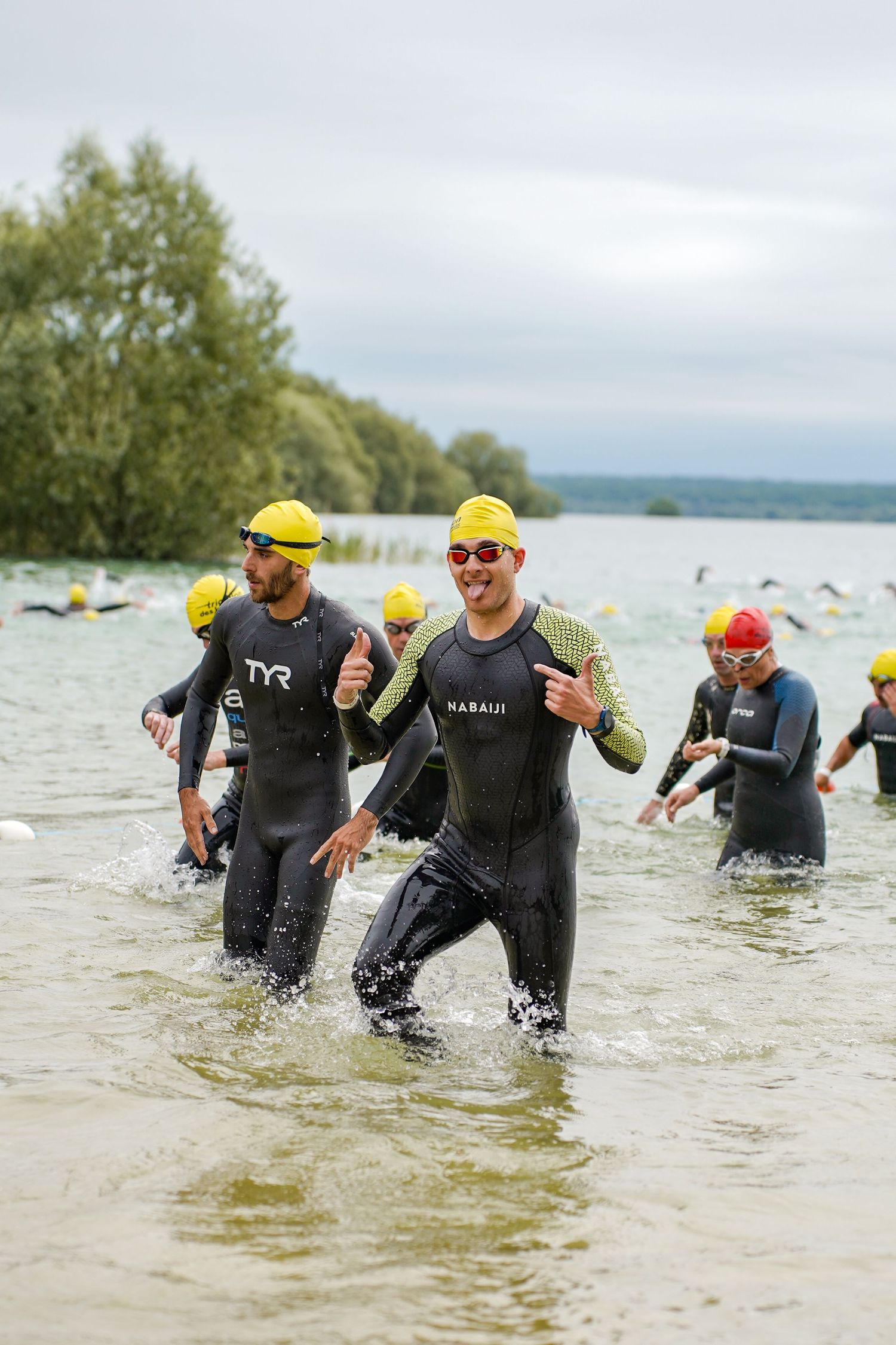 Athletes in wetsuits and yellow caps emerging from water during triathlon swim.