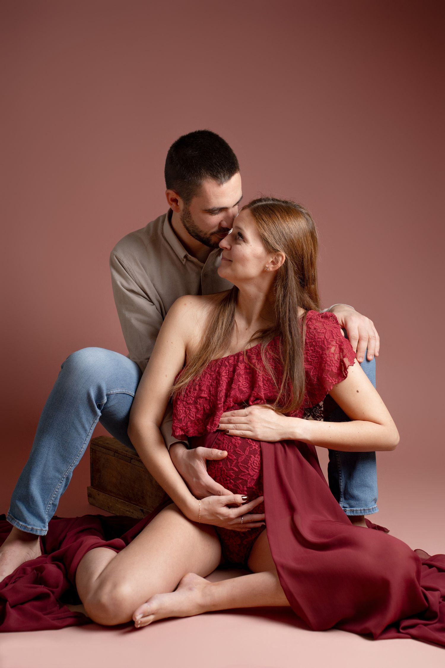 Intimate maternity photography session with couple in burgundy tones.