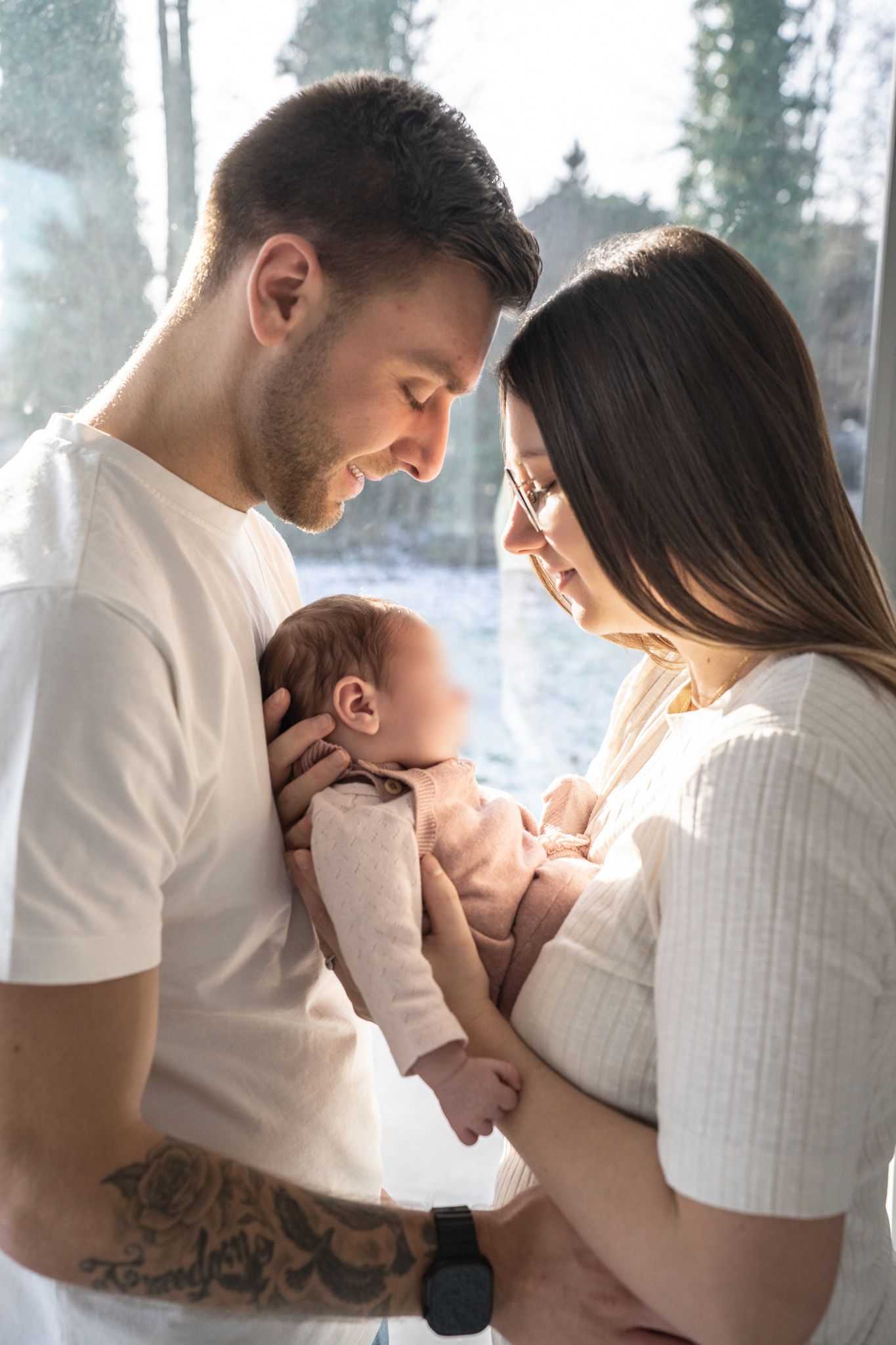 Intimate family moment with newborn baby by window in soft natural light.