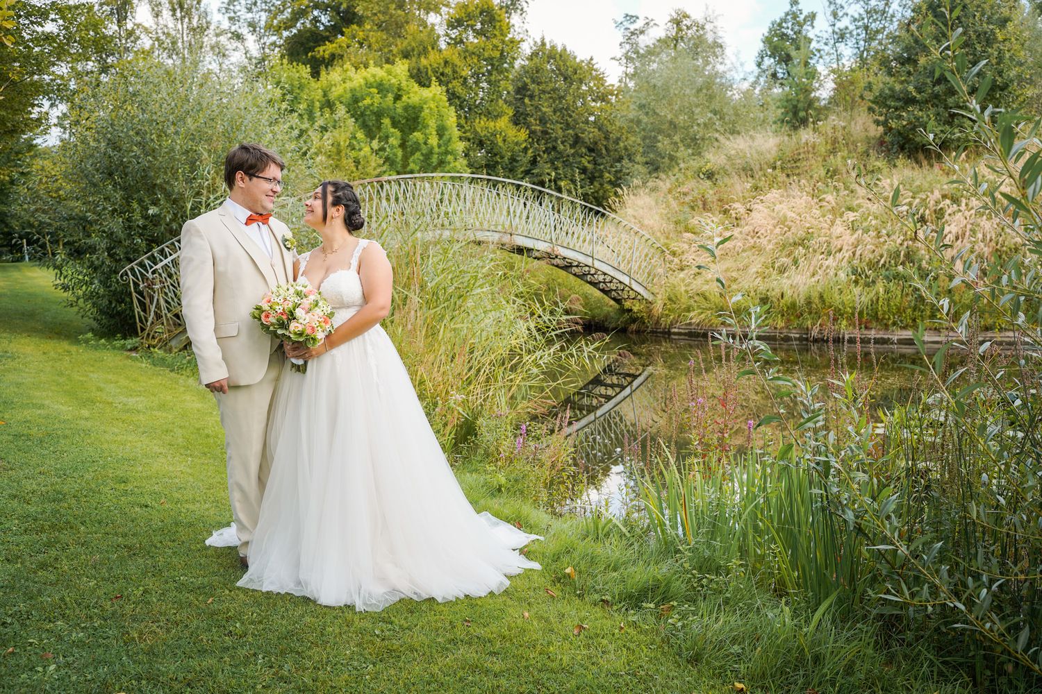 Wedding couple poses in a natural garden setting with tall grasses and trees.