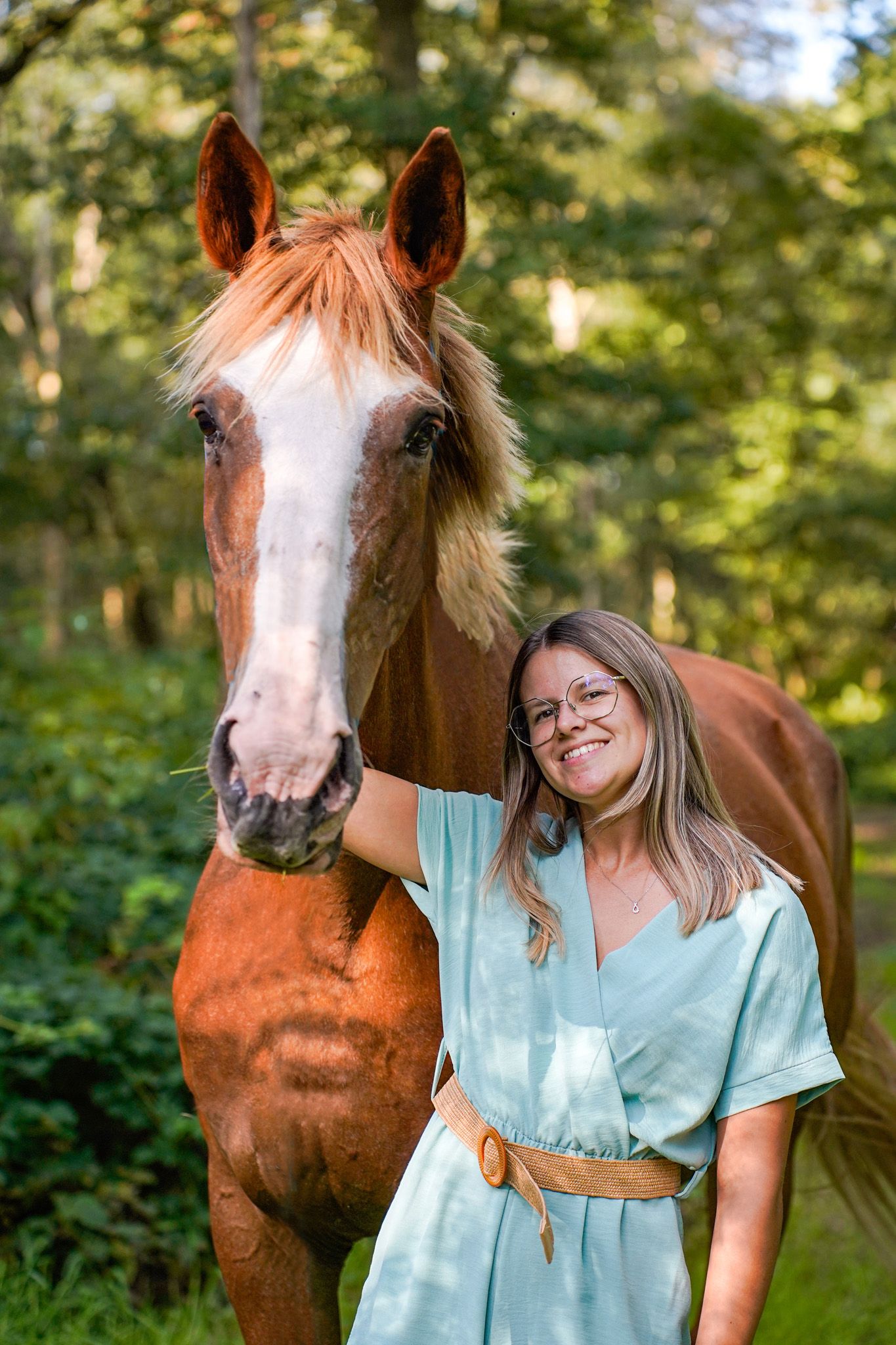 A beautiful chestnut horse and companion share a joyful moment in a sunlit forest setting.