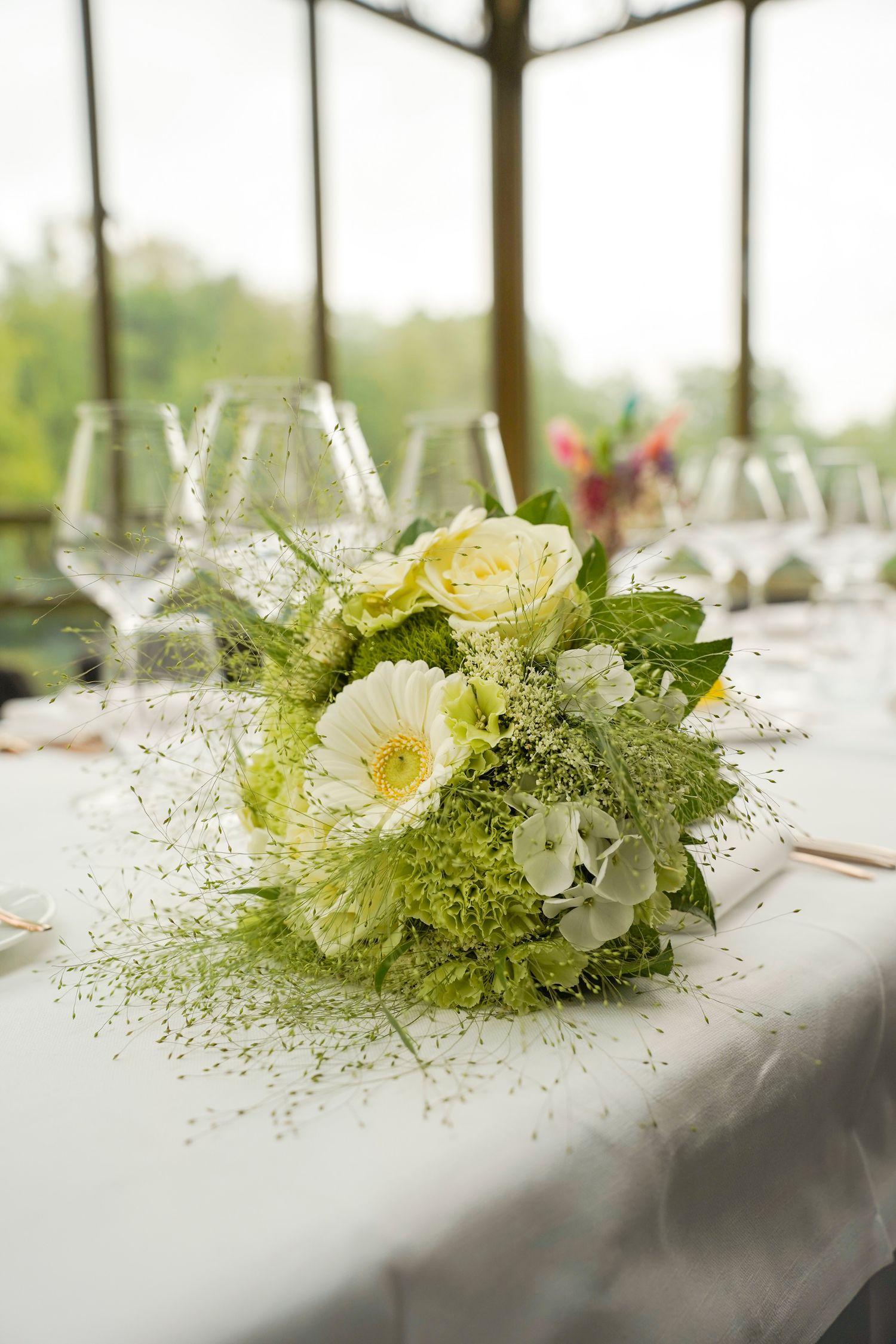 Elegant floral centerpiece with white and green flowers arranged on a white tablecloth.