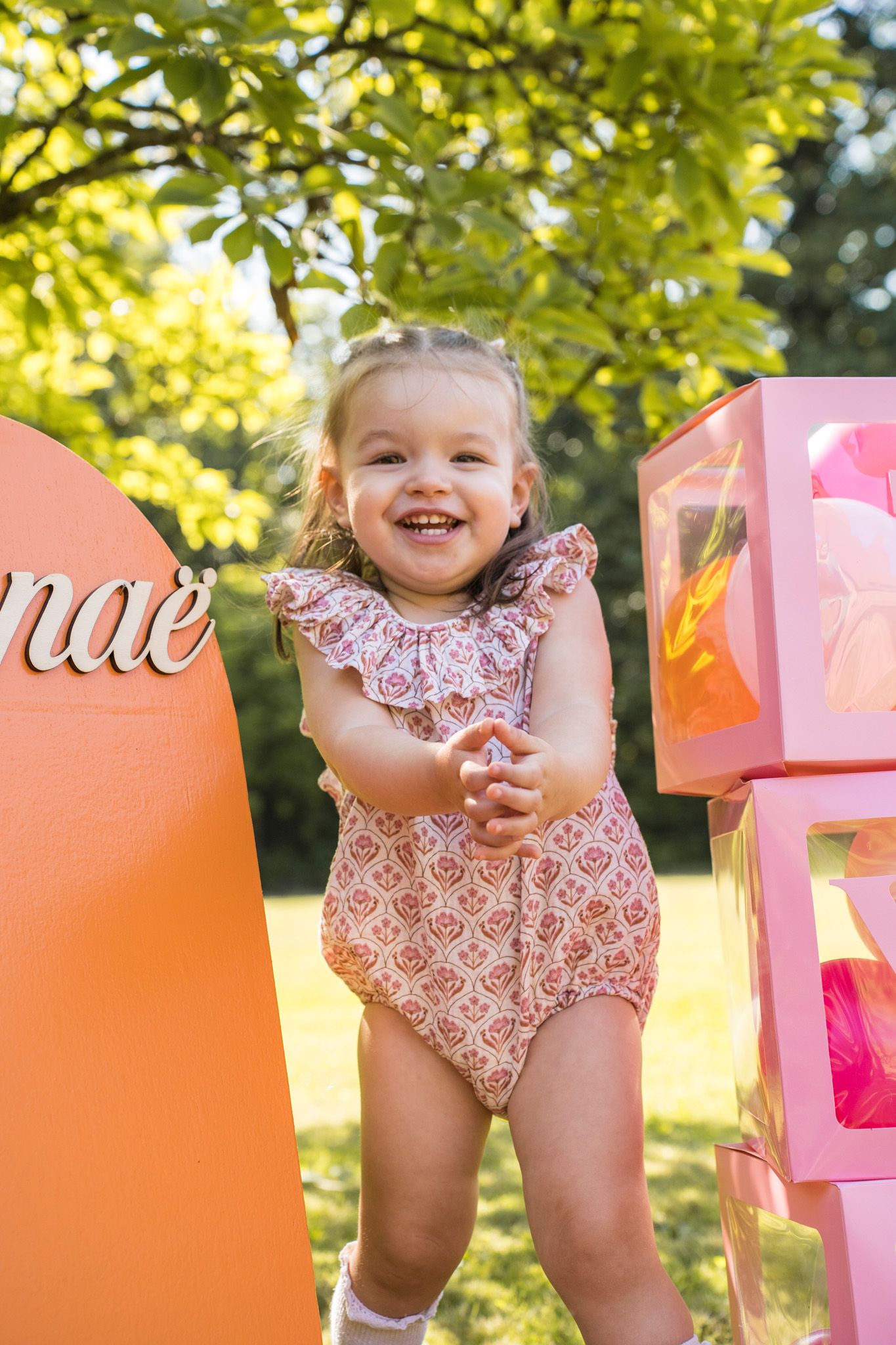 Colorful birthday setup with pink and orange balloons and decorative boxes in a sunny outdoor setting.