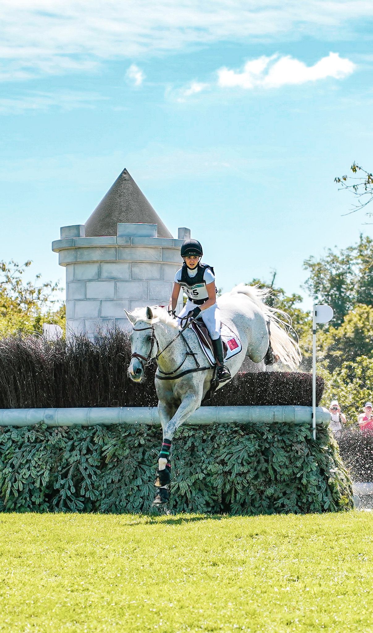 White horse and rider jumping over a decorative wall obstacle during an equestrian event.