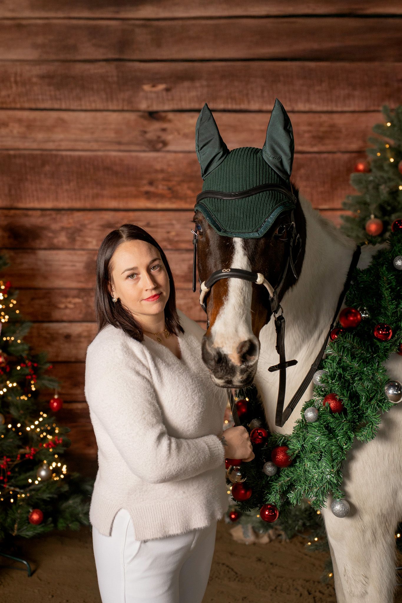Horse and rider pose for Christmas photos with decorated wreath and wooden backdrop.