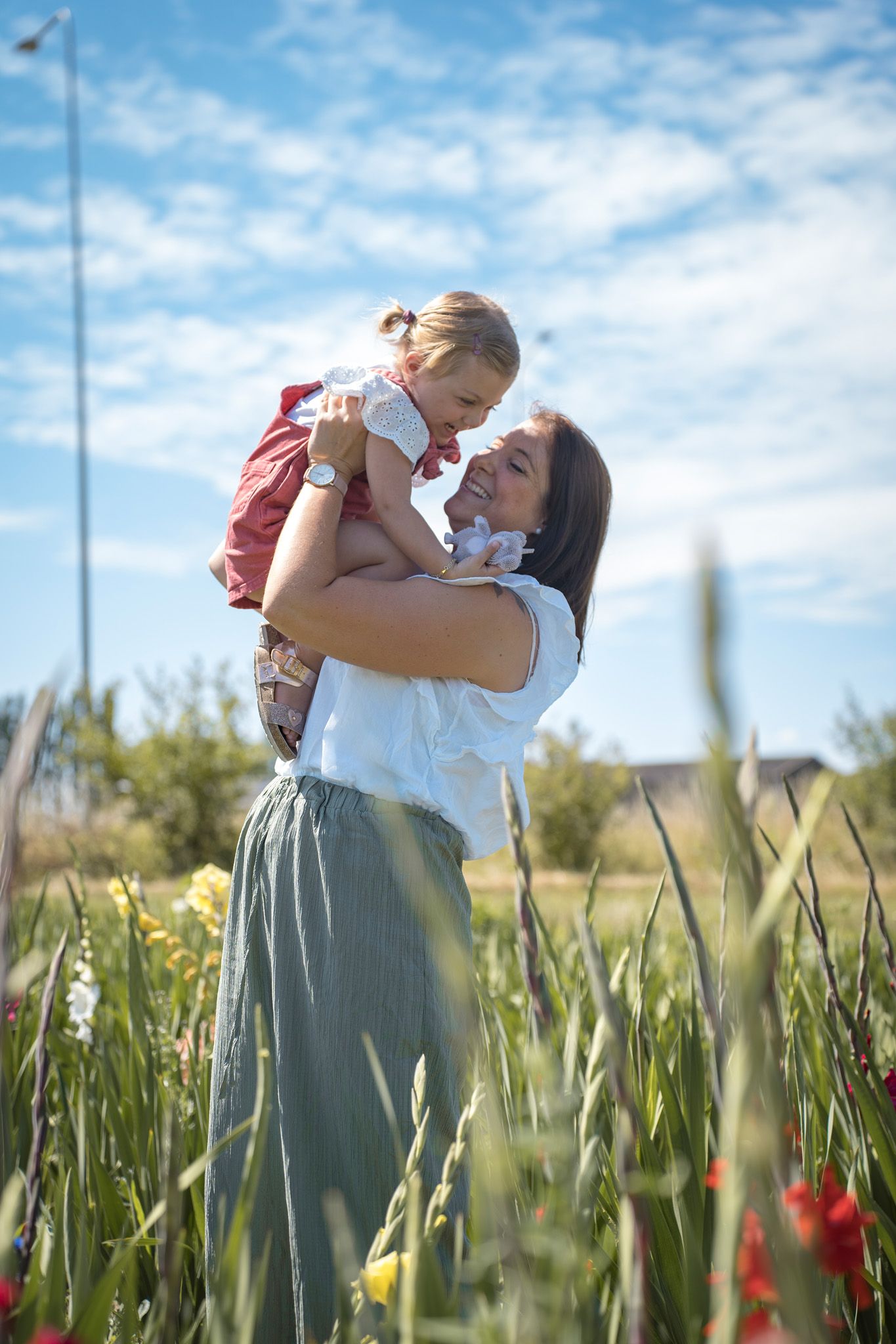 A tender moment shared in a field of wildflowers with red poppies under a bright blue sky.