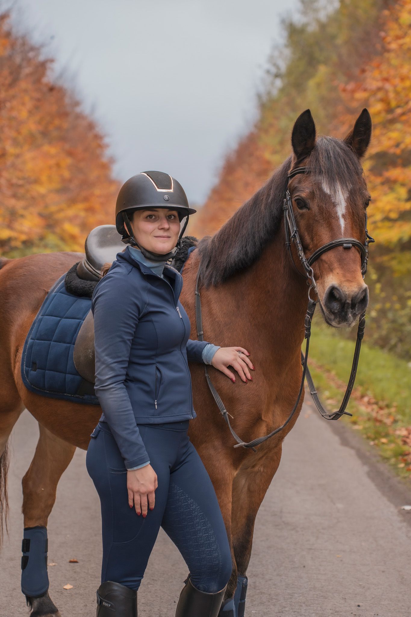 Horse and rider on autumn path lined with colorful fall foliage.