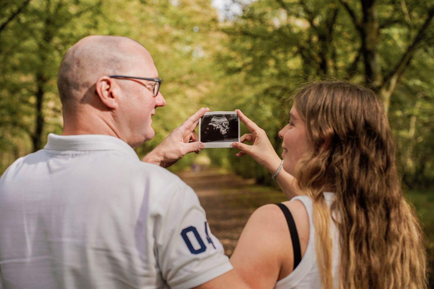 Romantic maternity photos captured in a natural outdoor setting with trees in background.