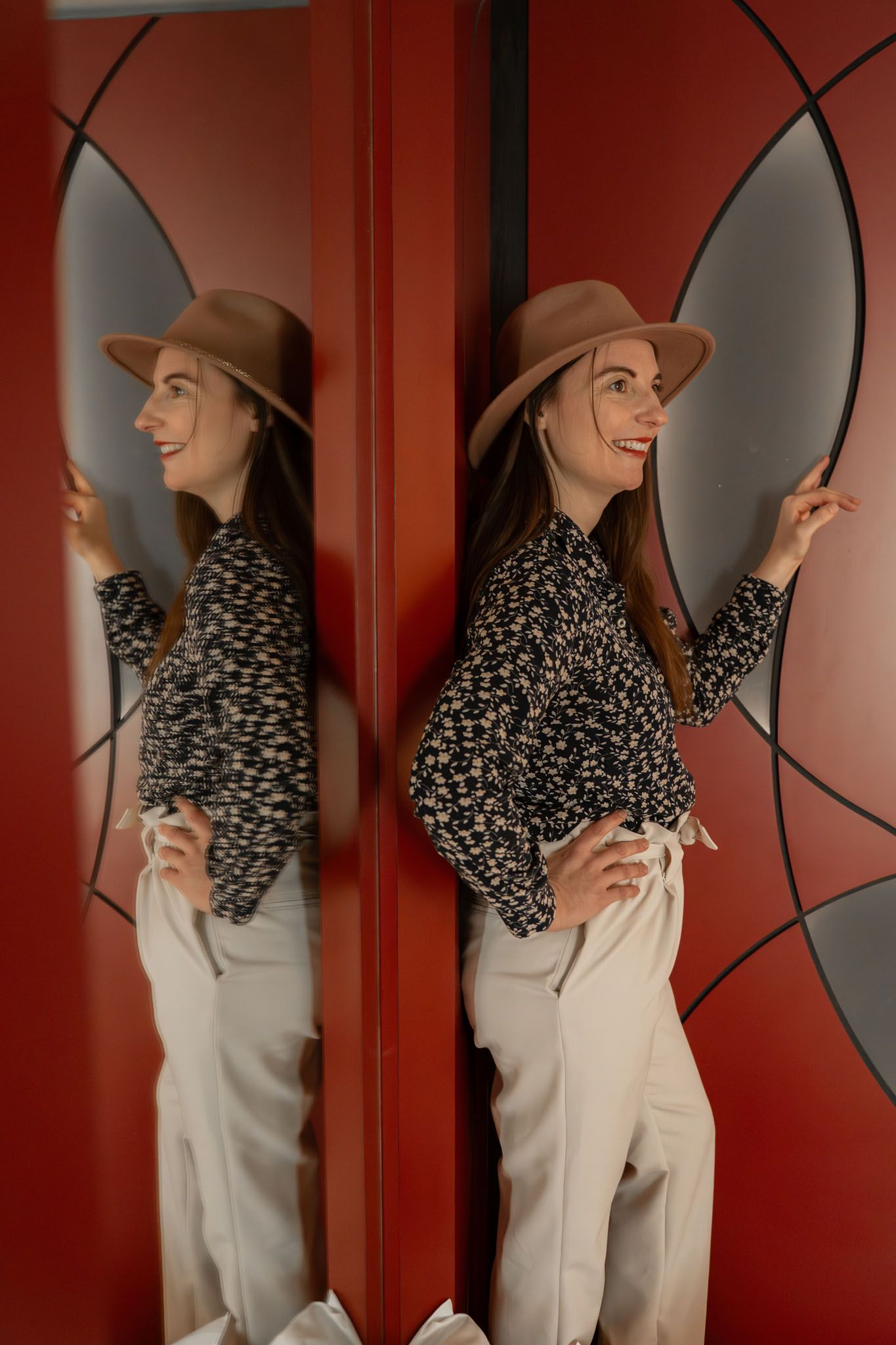 Person in patterned top and hat posing against geometric red wall design.