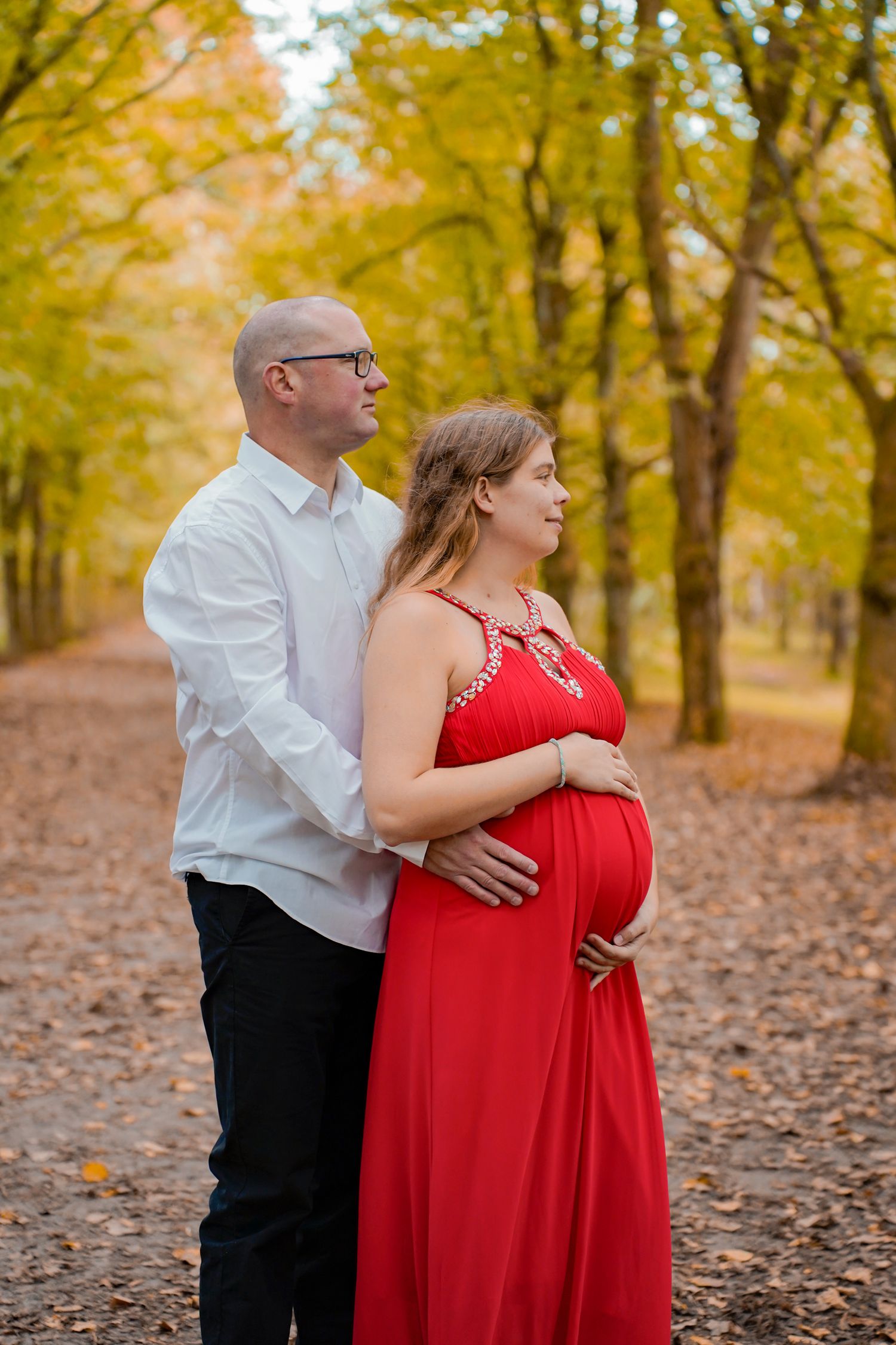 Maternity photos showing couple embracing in a golden autumn forest setting.