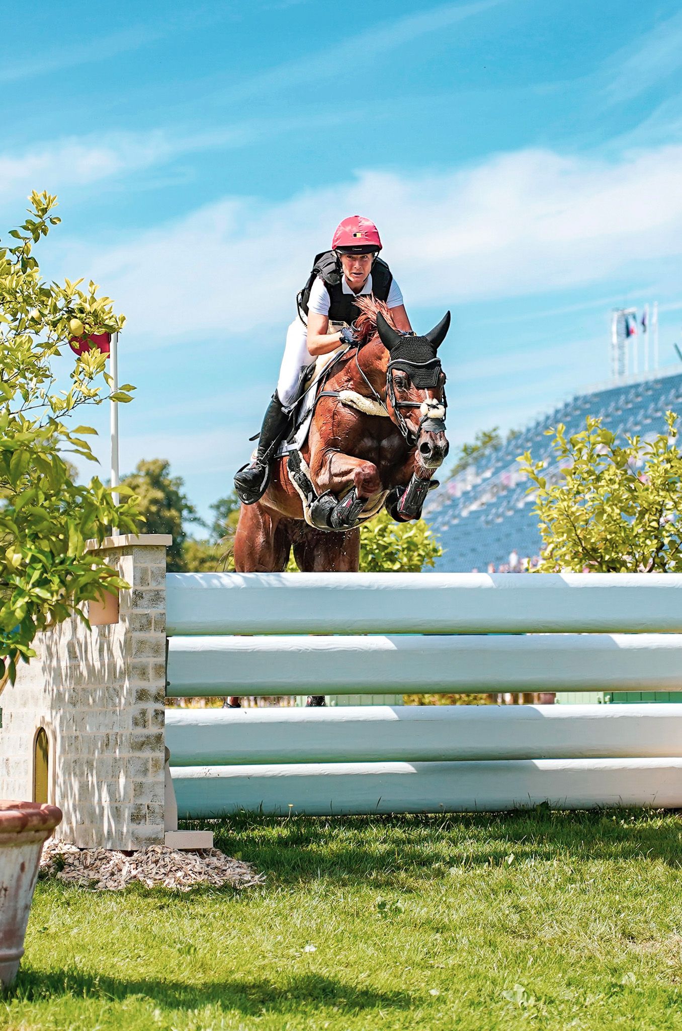 Horse and rider clearing a high white show jumping fence against blue sky.