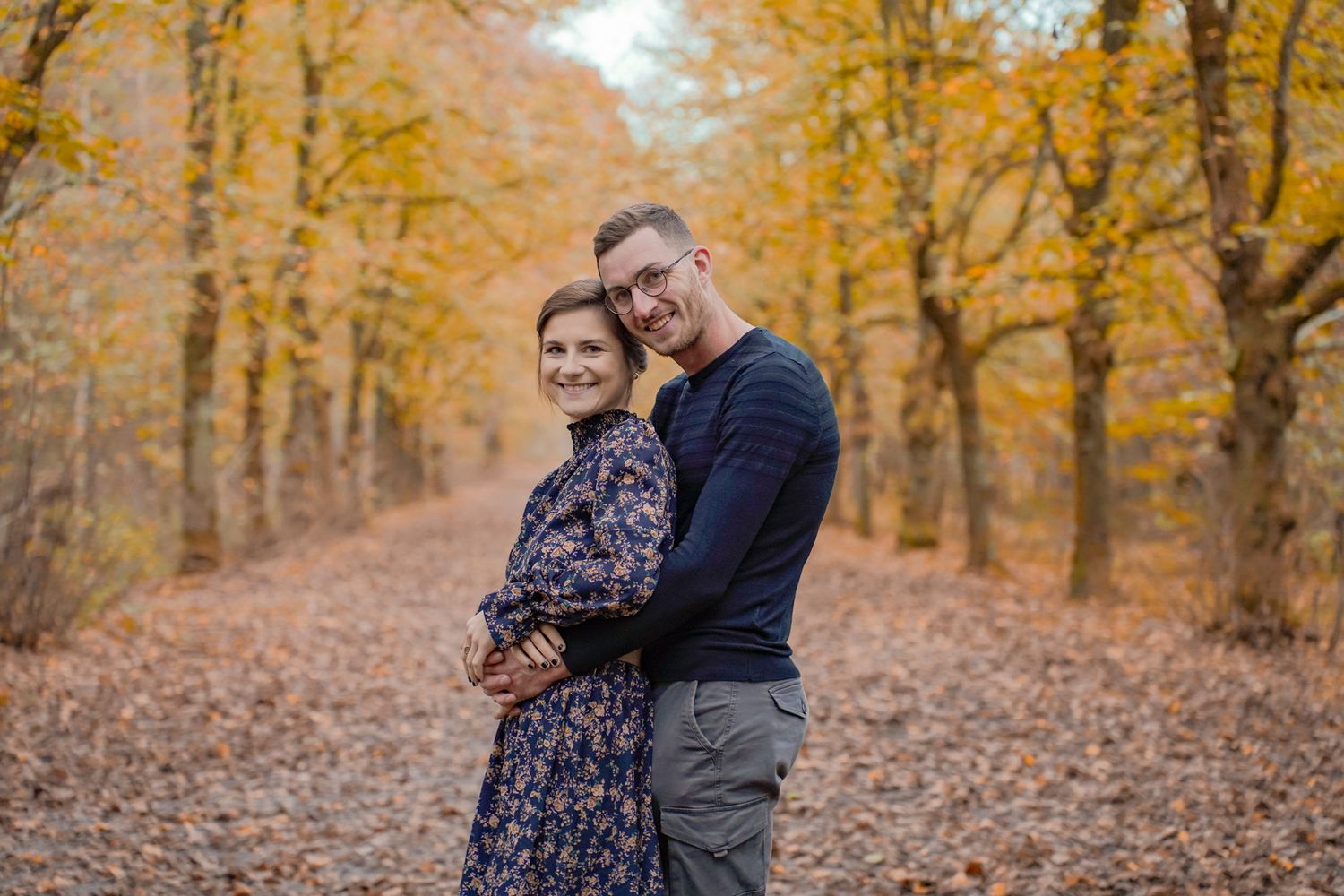 Romantic couple photography session in a forest with warm fall colors and fallen leaves.