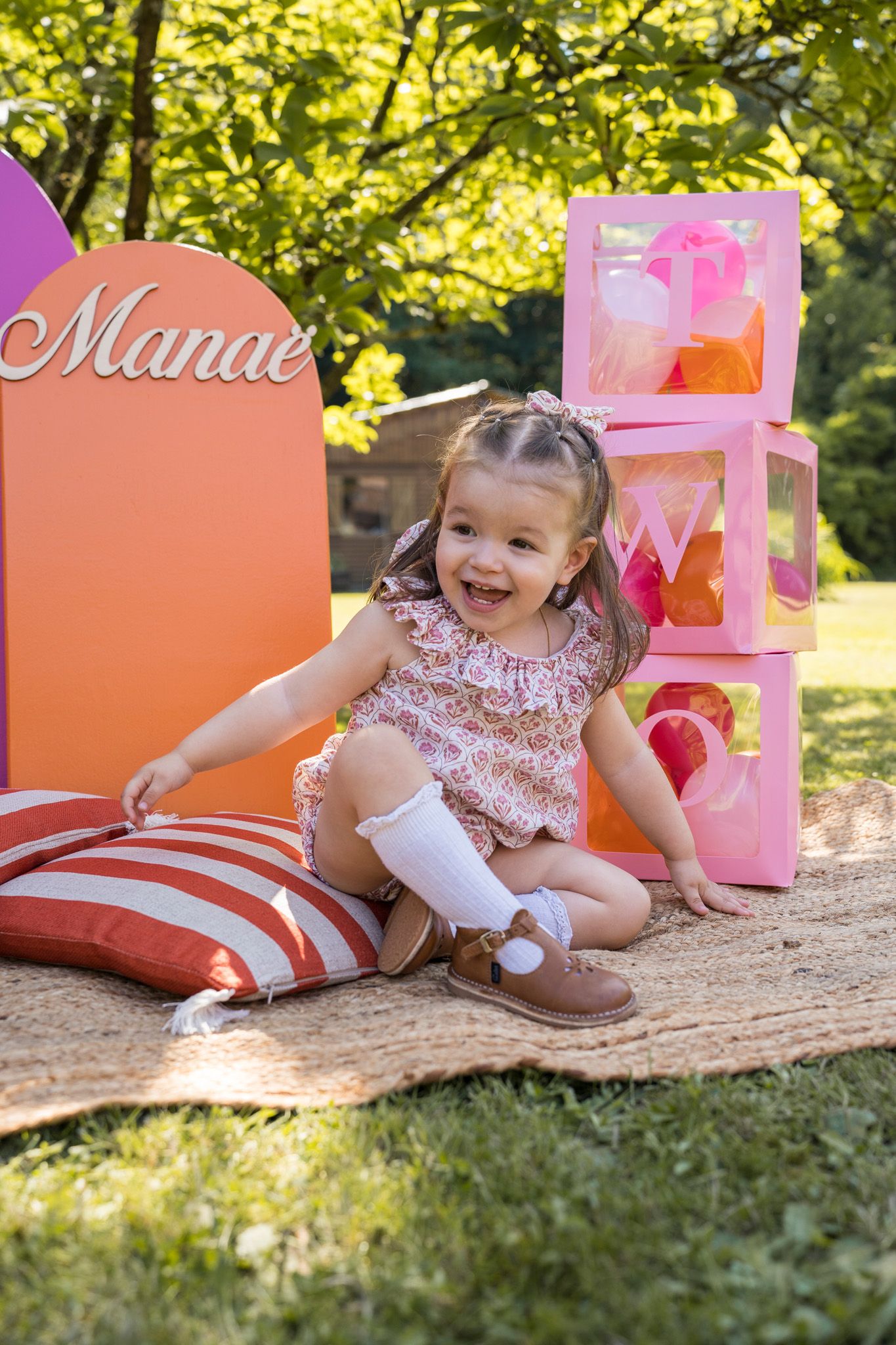 Birthday party setup in a garden with pink decorations and striped blanket.