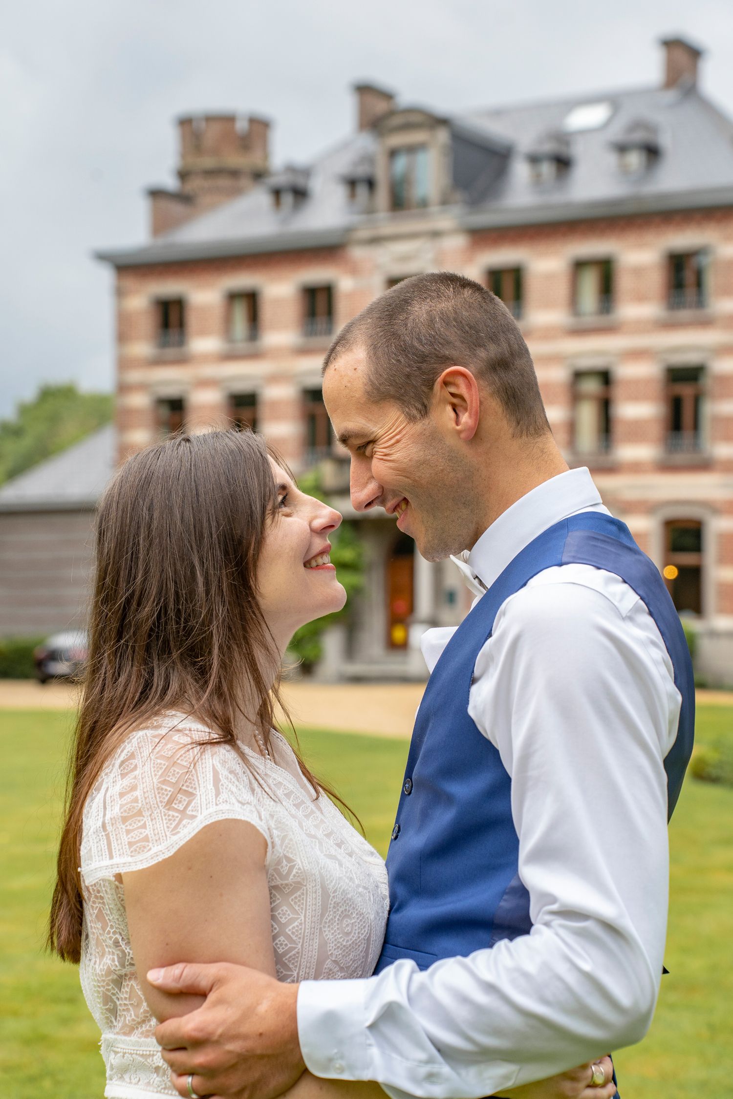 Couple shares intimate moment on lawn with historic estate building in background.