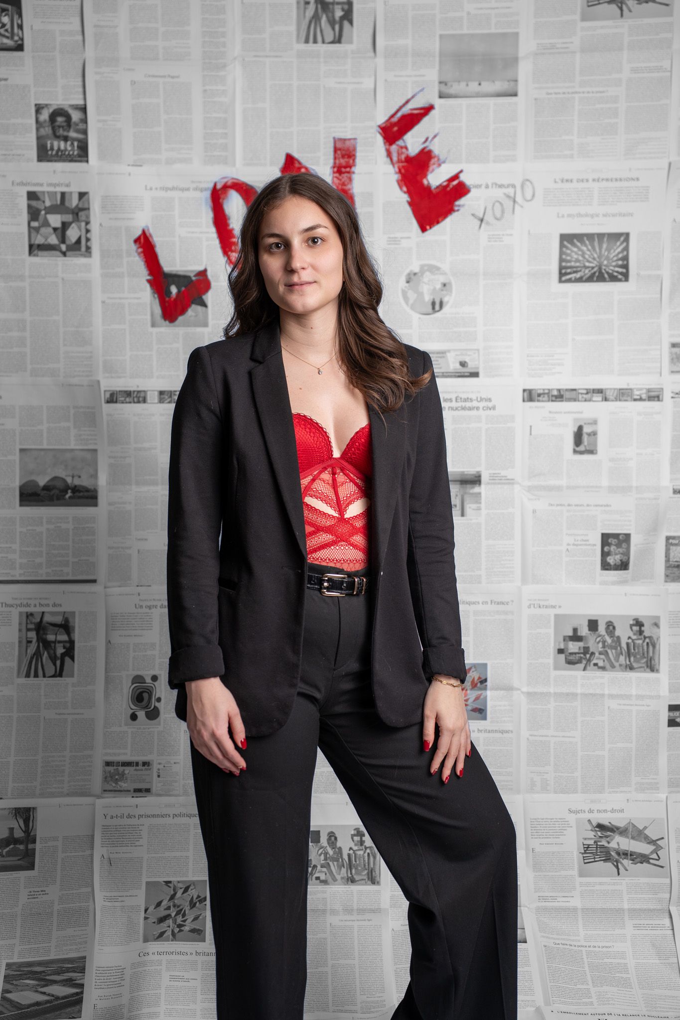 Fashion portrait series of woman in black suit against newspaper wall with red Valentine's decorations.