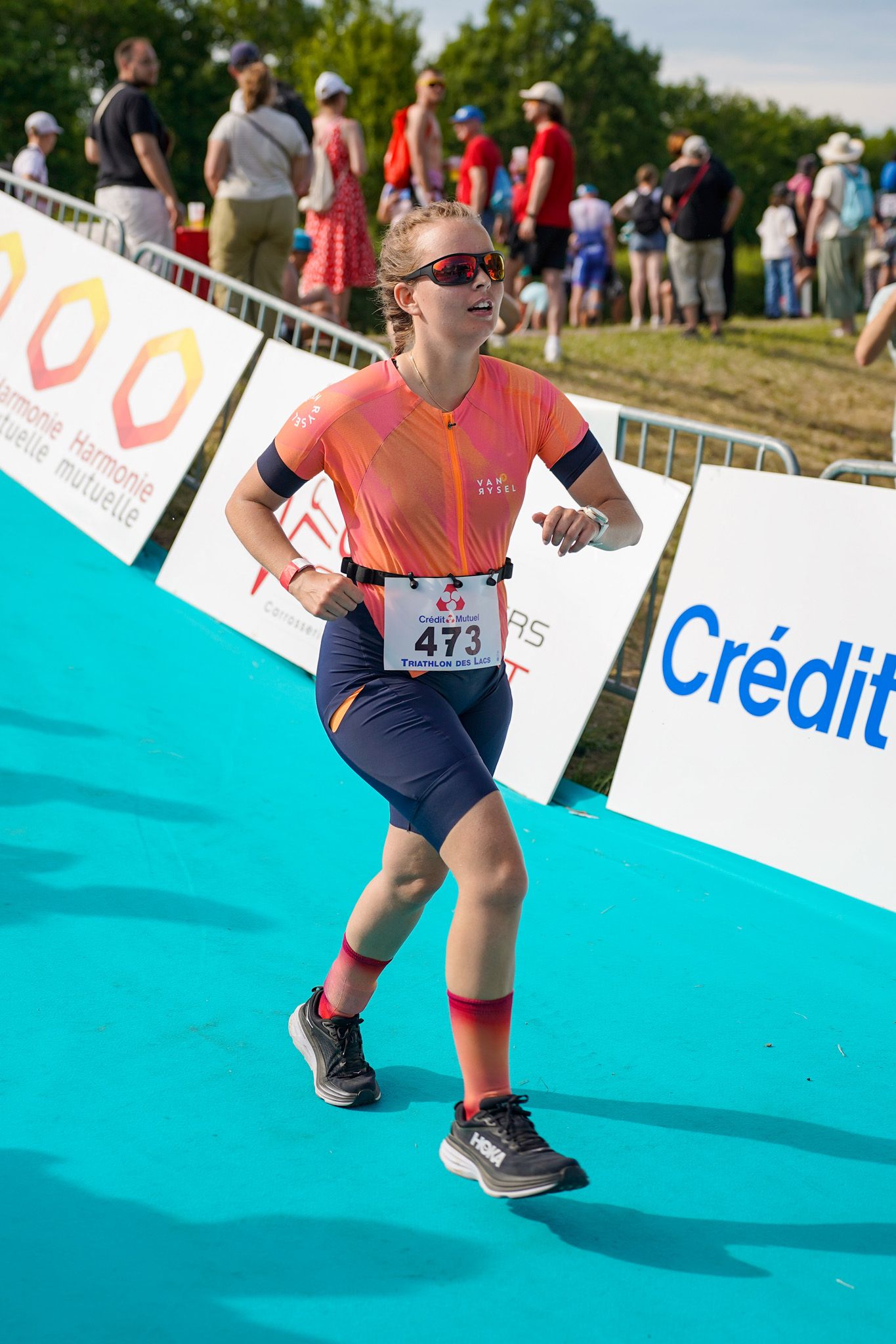 Athlete in orange jersey runs on turquoise track during competitive sporting event.