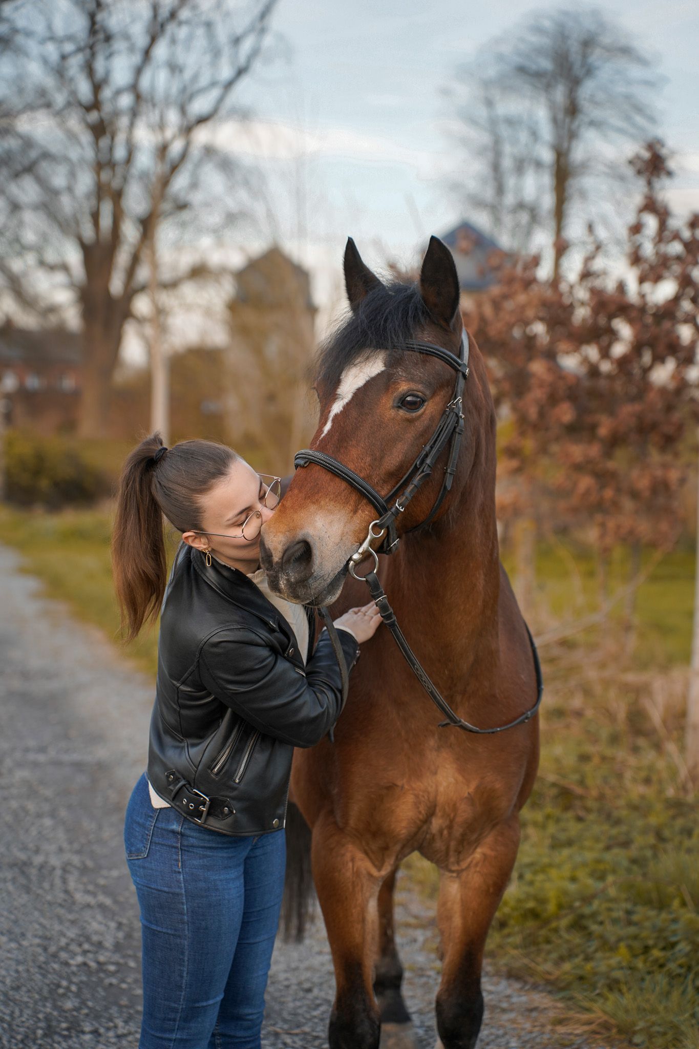 A brown horse receives affection on a path with autumn trees in the background.
