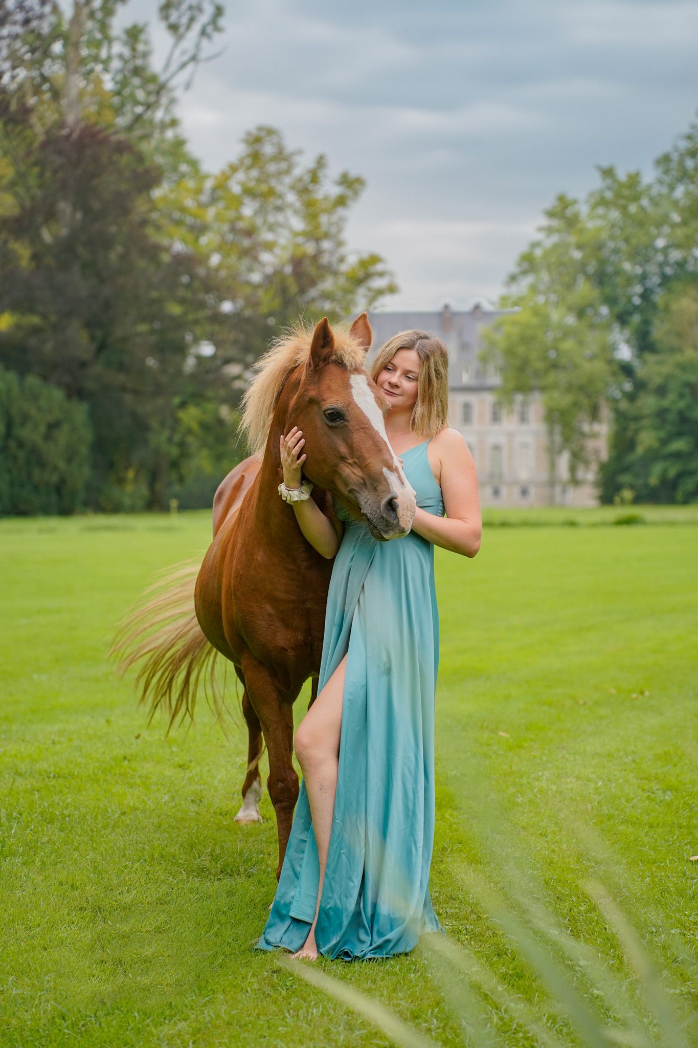 Horse and companion in turquoise dress posing on manicured castle grounds.