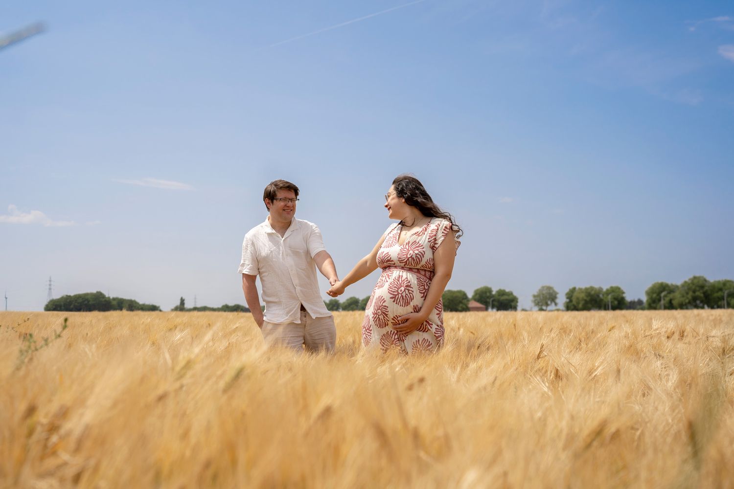 Couple walks together through golden wheat field on bright summer day.
