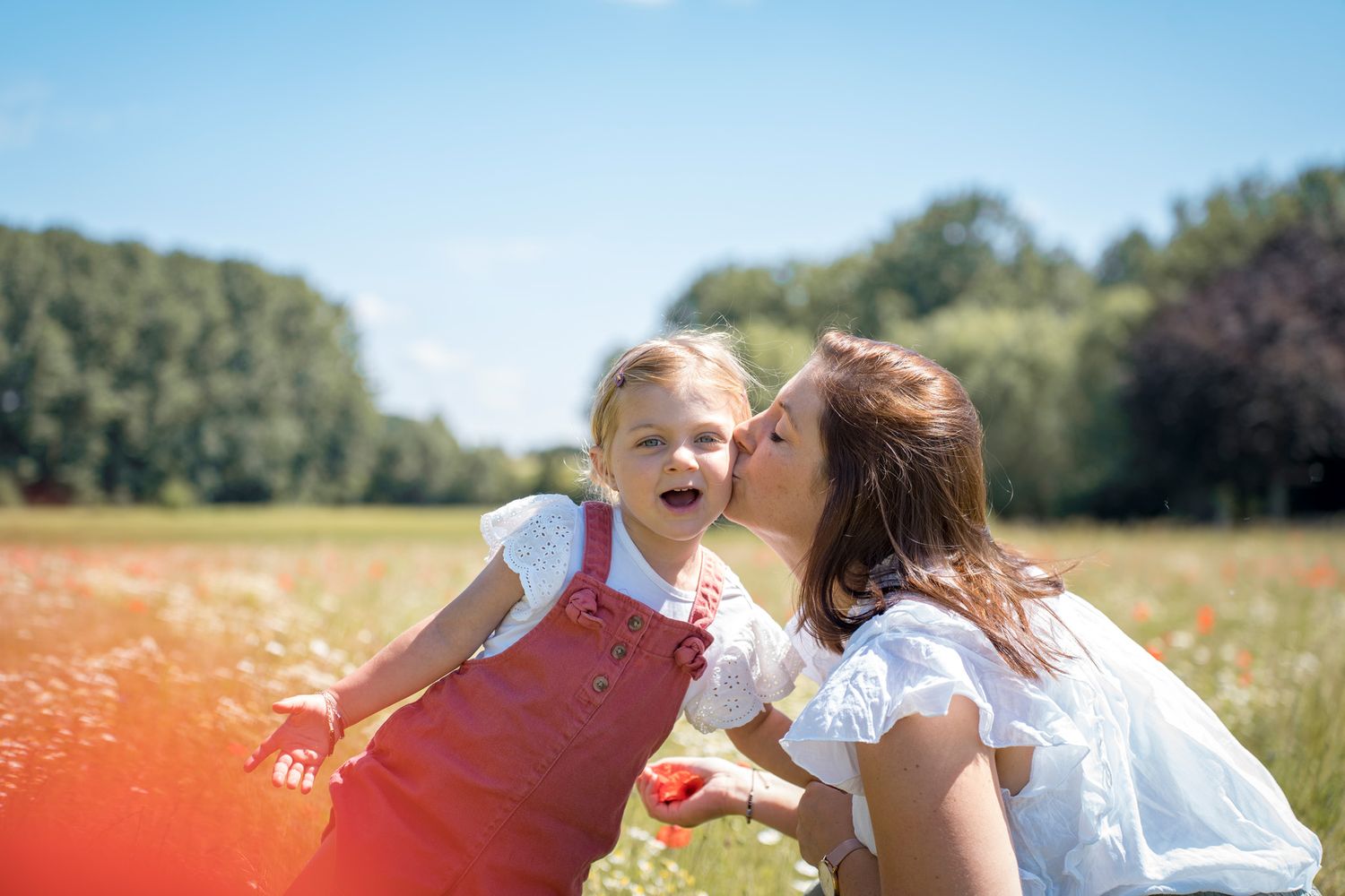 Joyful moments captured in a sunlit meadow with wildflowers and trees in the background.