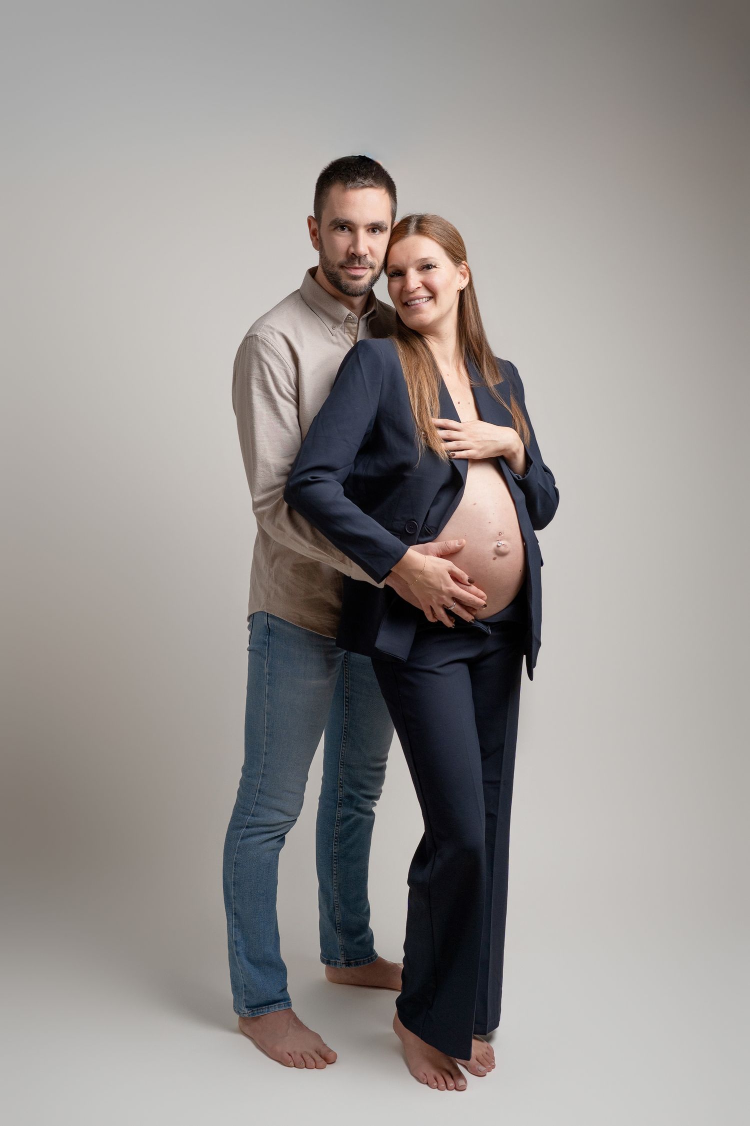 Studio maternity session with couple in casual business wear.