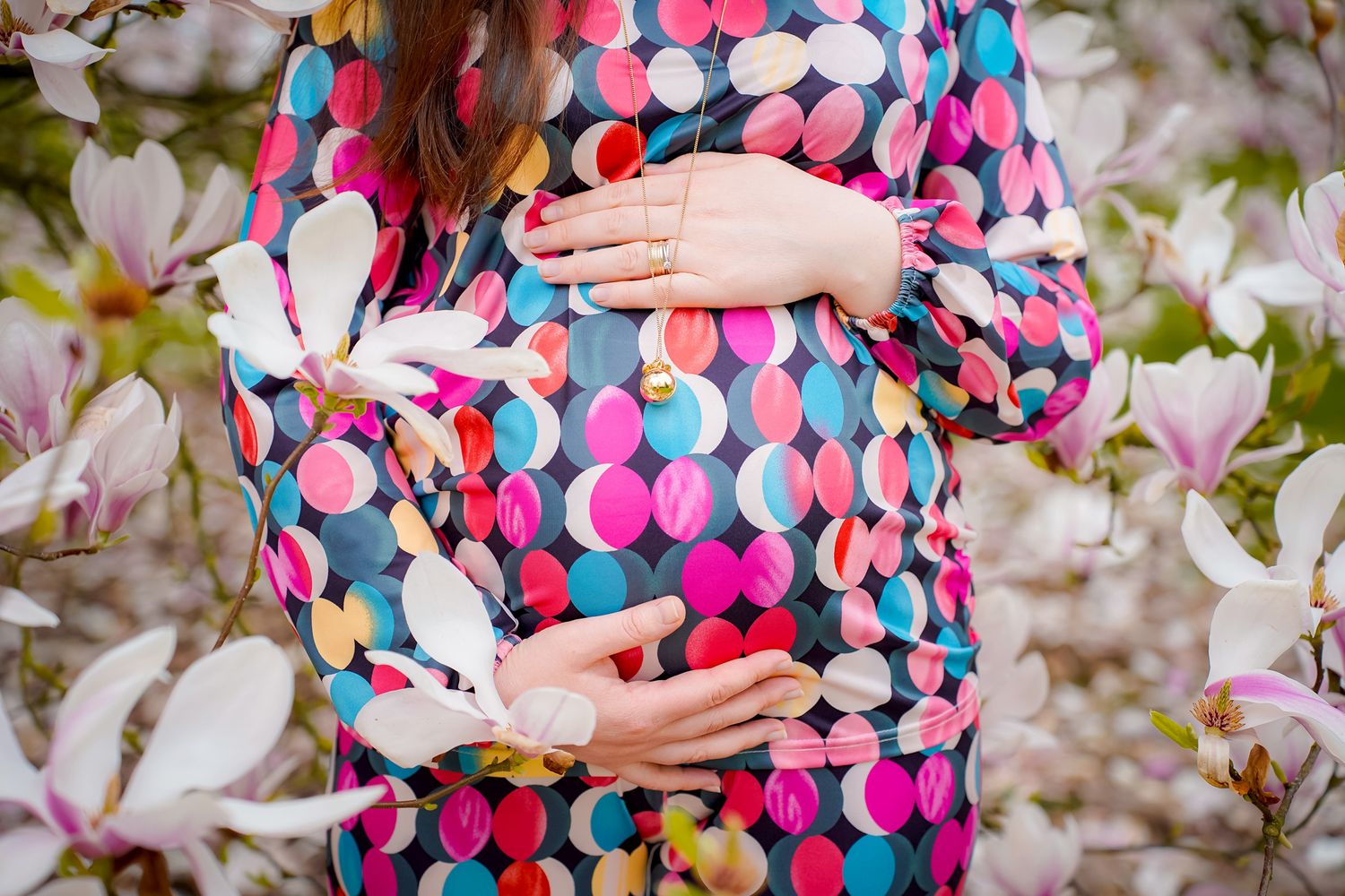 Close-up of a pregnant belly in a colorful polka dot dress among spring blossoms.