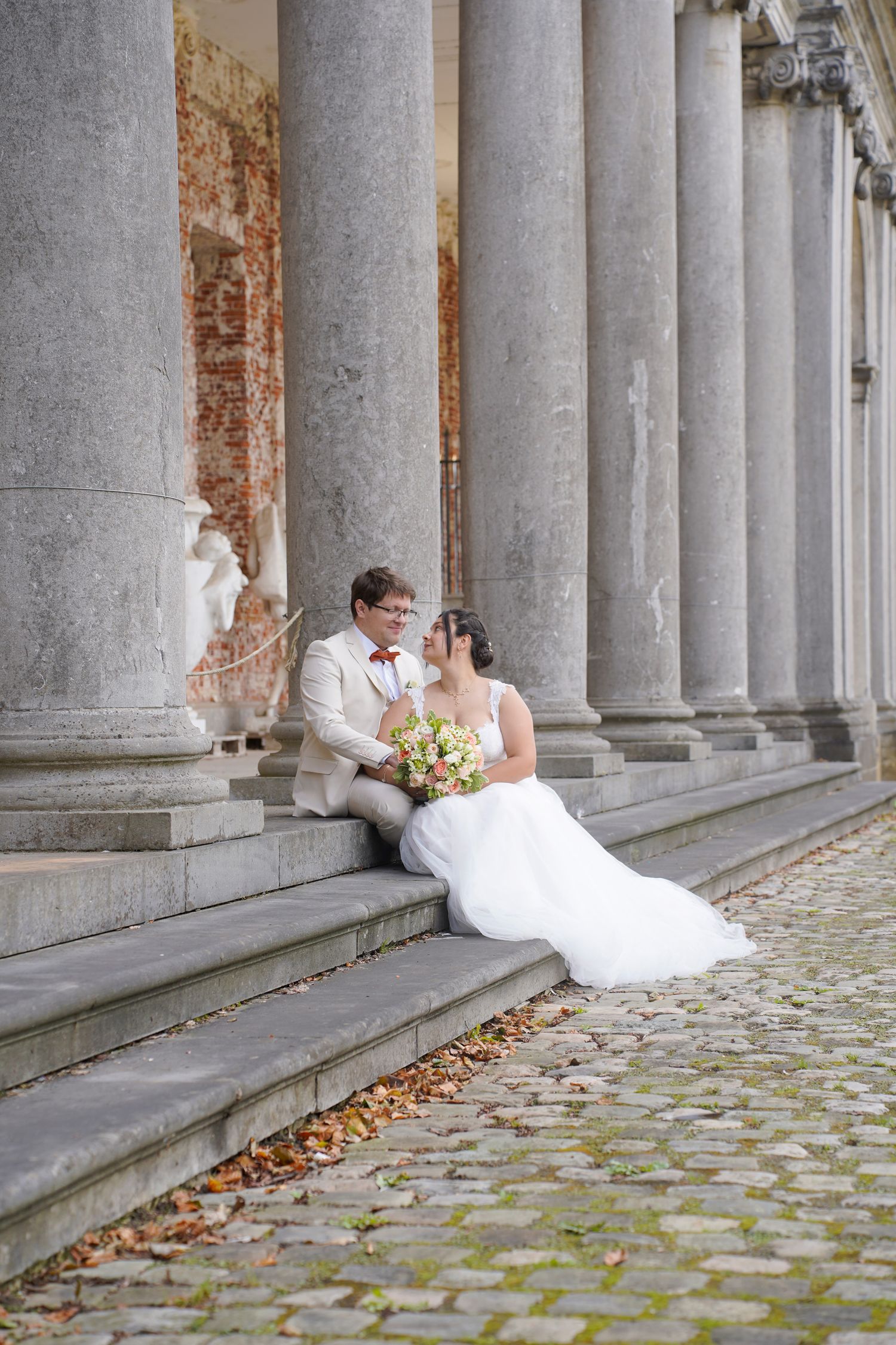 Wedding portraits taken along a historic colonnade with weathered stone pillars.