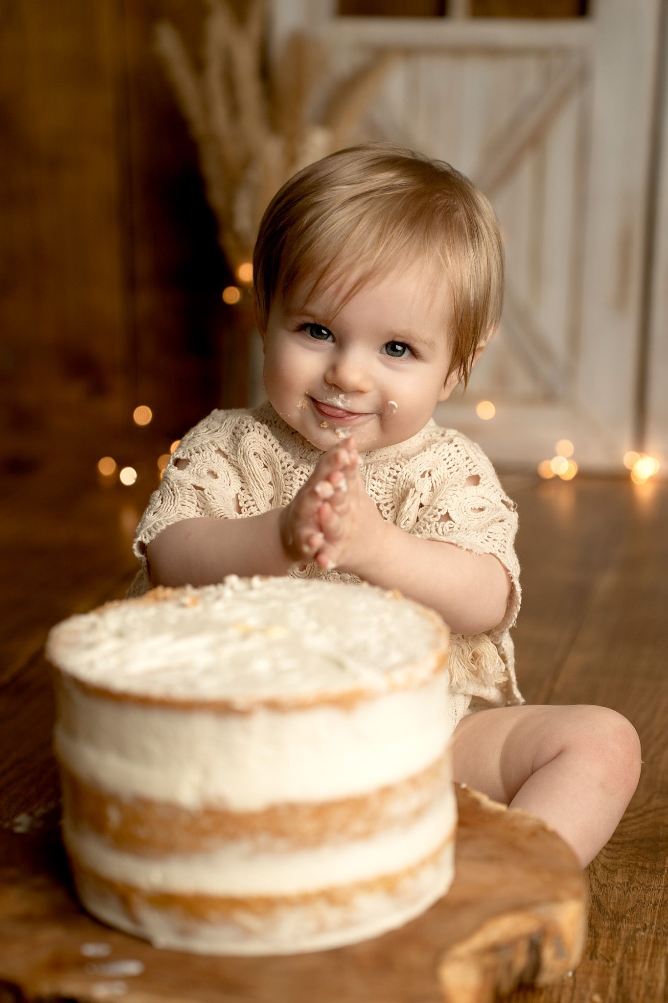 White frosted cake on wooden table with twinkle lights in background.