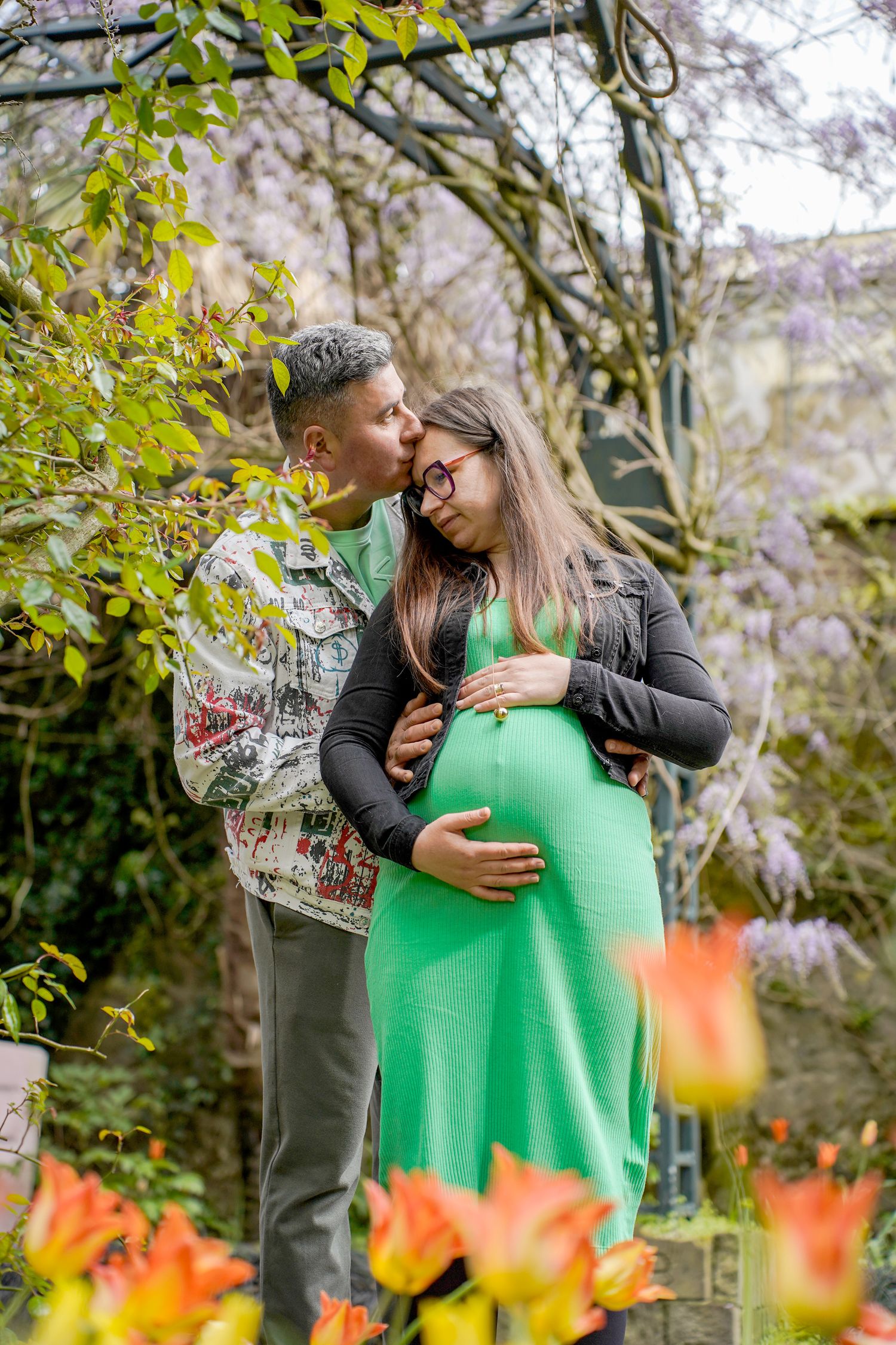 Romantic maternity photo in a garden with purple and orange flowers in the foreground.