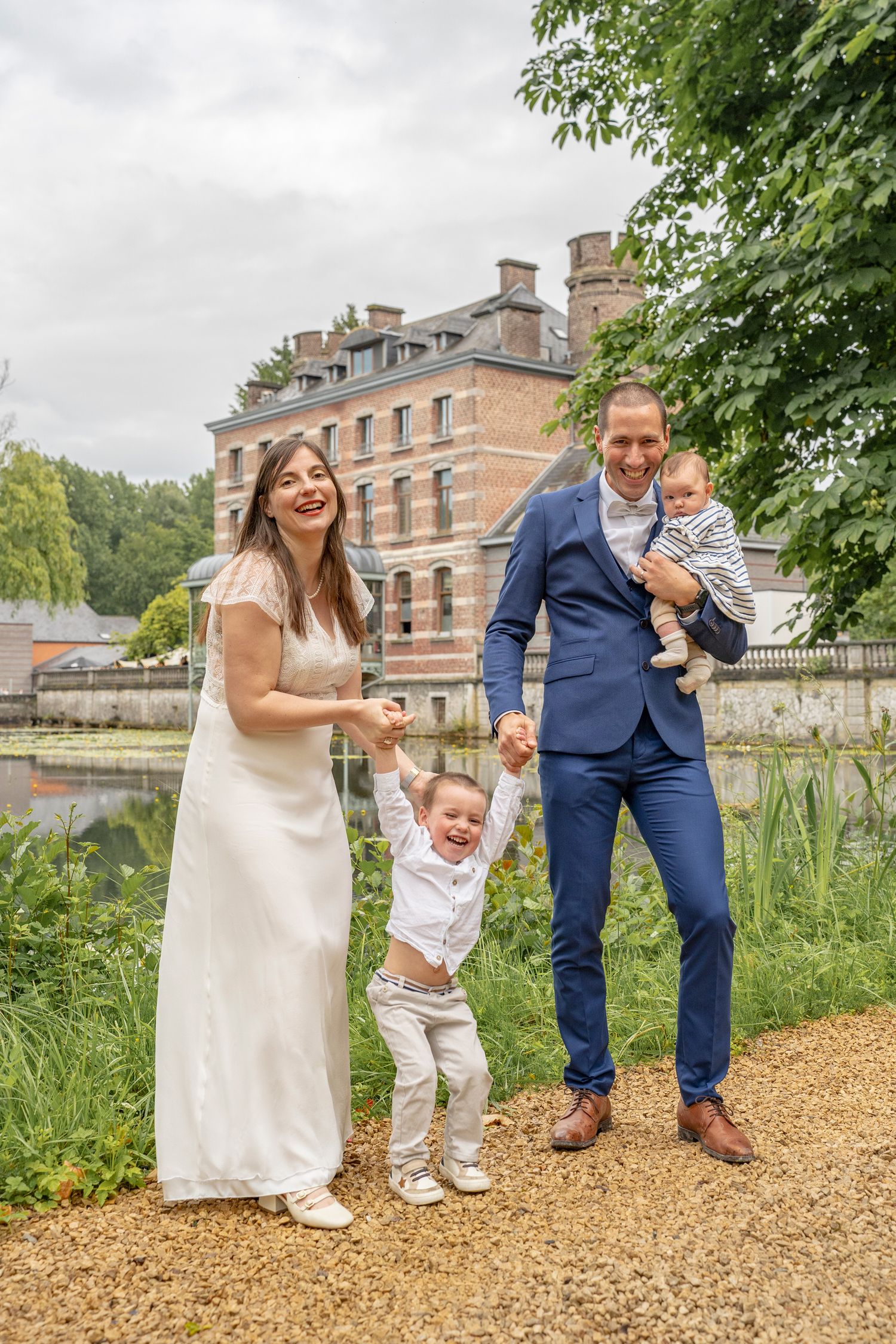 Family enjoying playful moments together on path near historic mansion and pond.