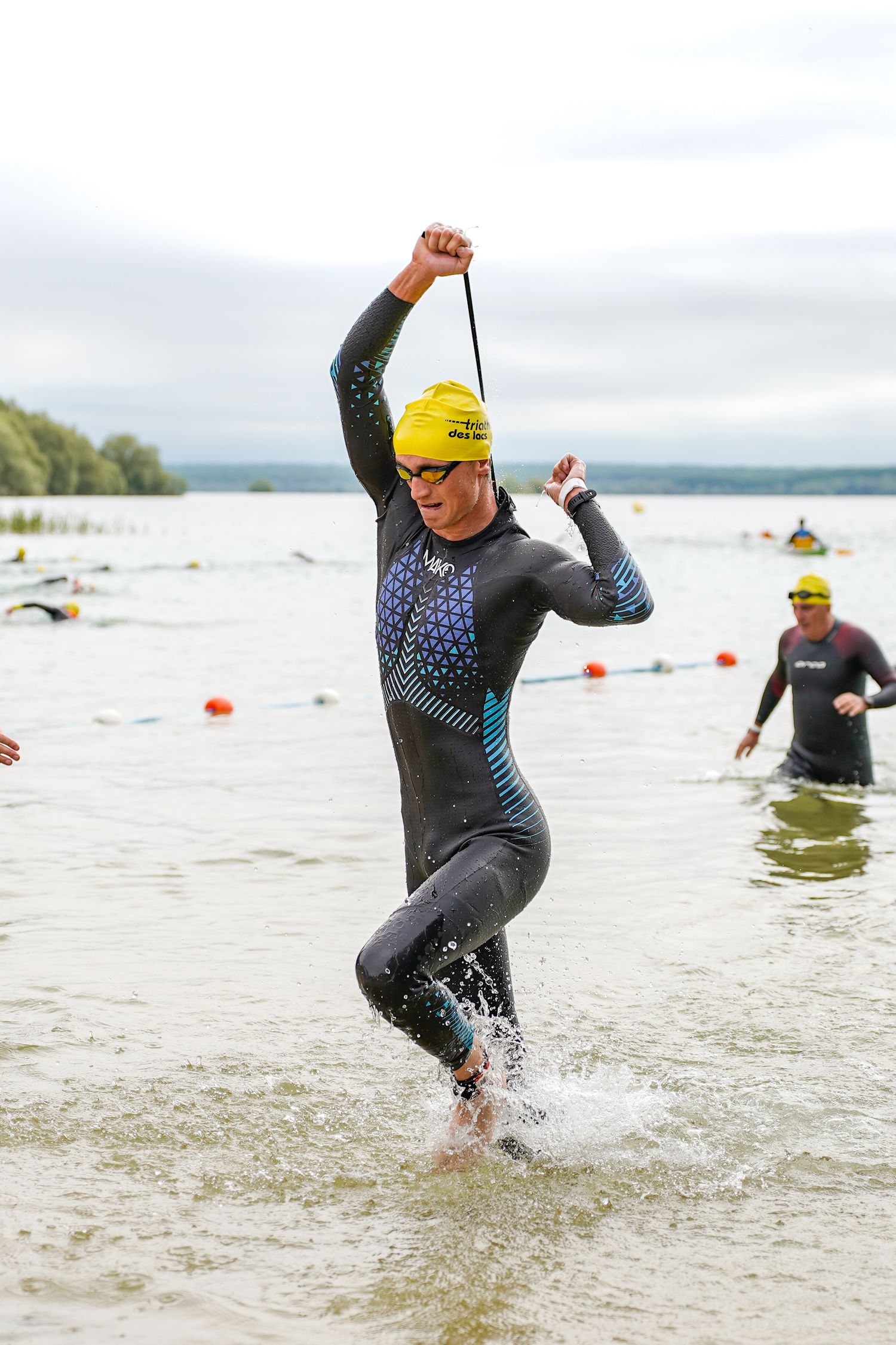 Athlete in wetsuit and yellow cap splashing through water during triathlon swim.