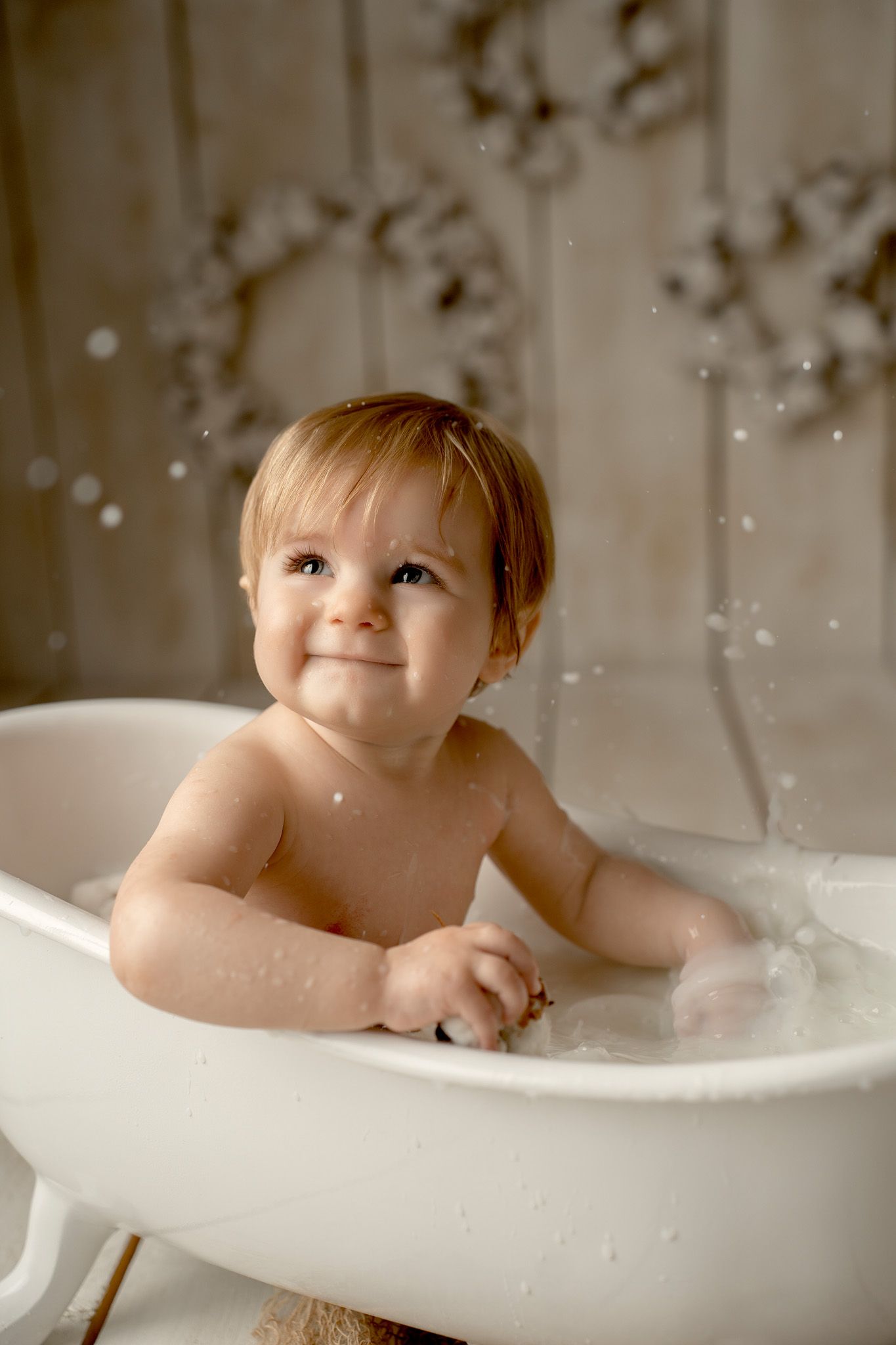 Baby plays in a vintage white clawfoot bathtub during a playful photo session.