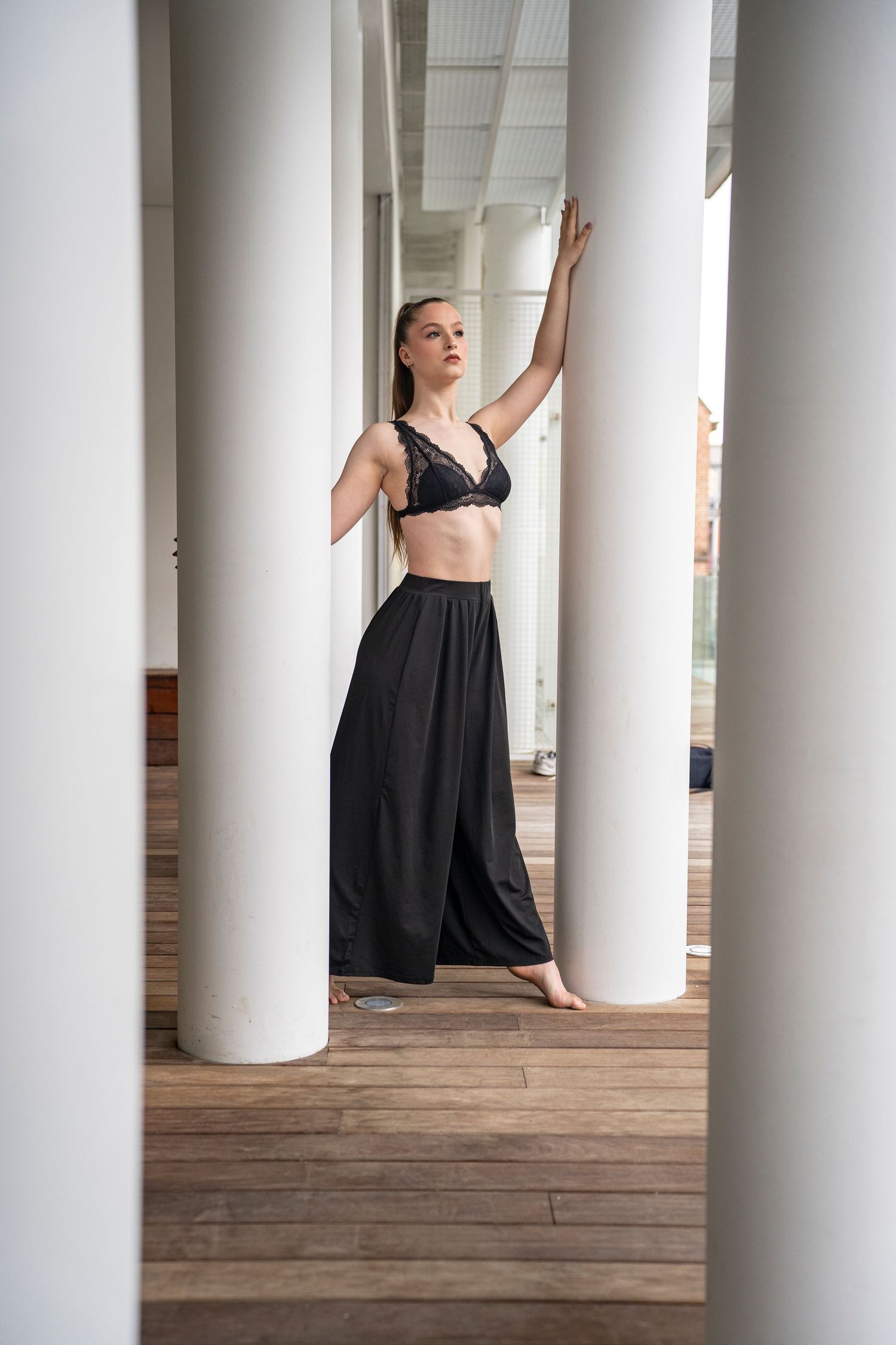 A dancer in black moves elegantly between white columns in an architectural setting.
