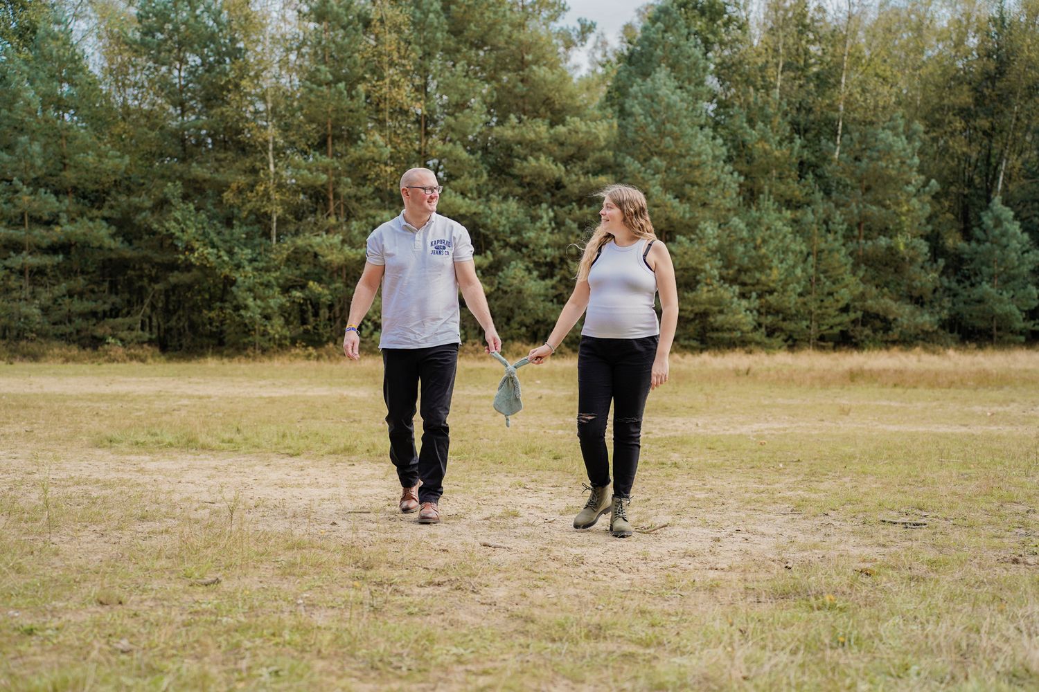 Couple walking hand in hand through a scenic field during their maternity session.