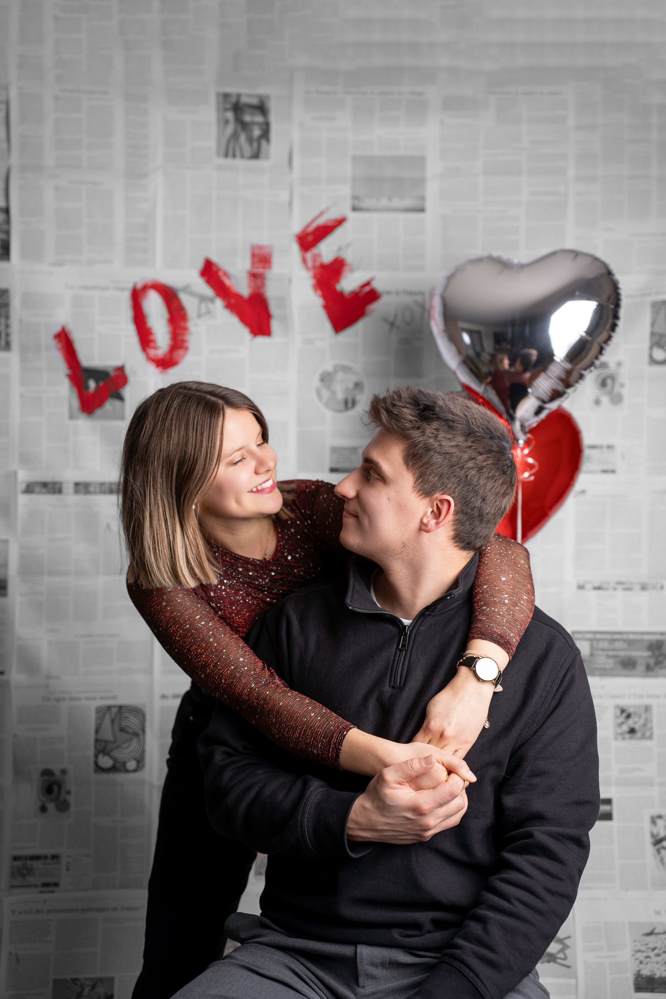 Couple shares intimate moments in black and white photo series with red heart balloons and newspaper backdrop.
