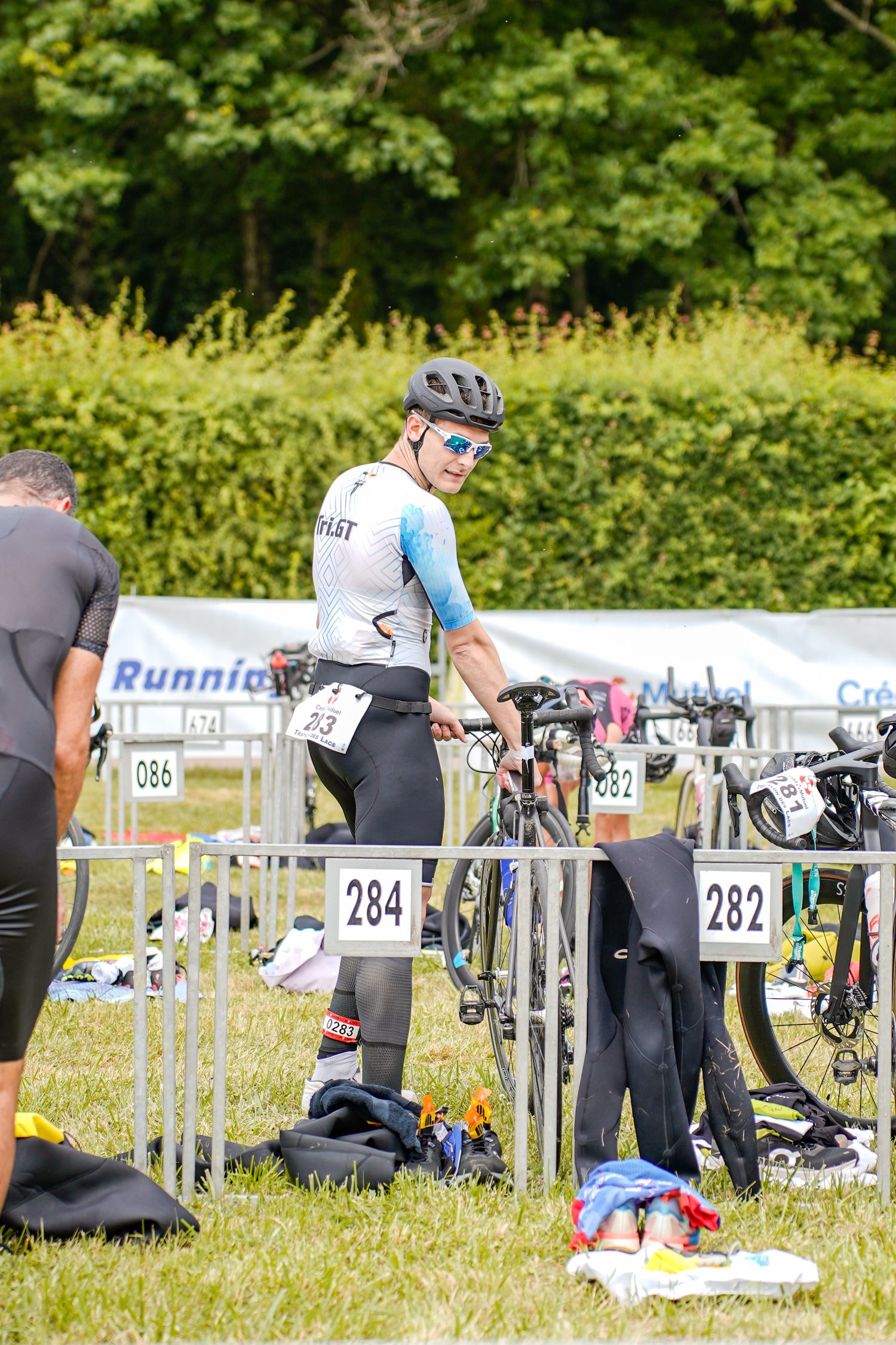 Transition area at triathlon event with bikes and gear racks set up on grass field.