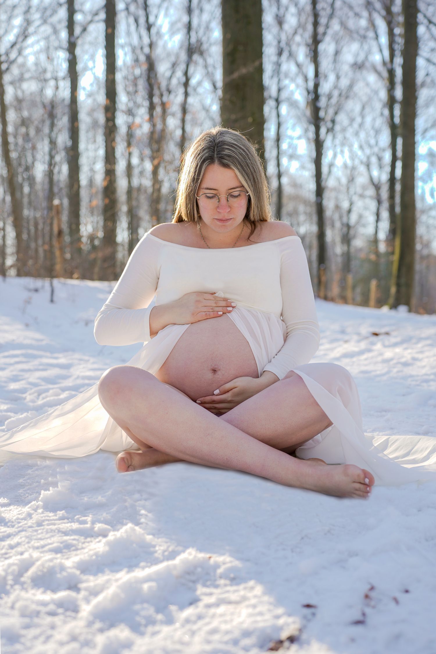 Artistic maternity photos on snow-covered ground with bare winter trees in background.
