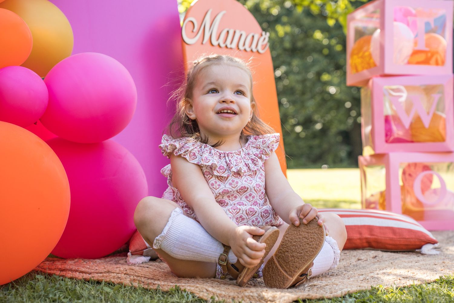 Pink and orange party decorations arranged outdoors with balloons and gift boxes.