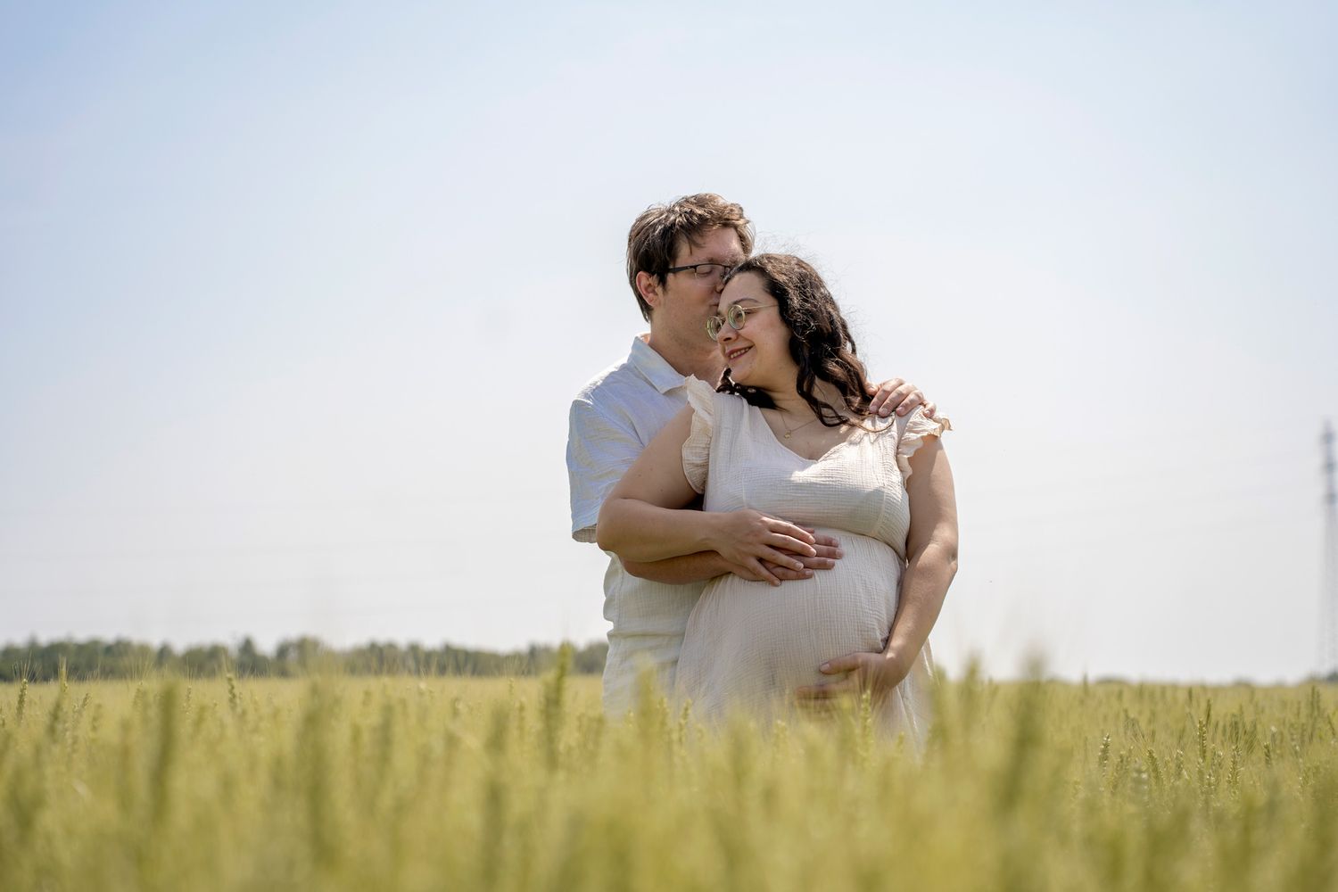 Couple shares tender moment while standing in sunlit wheat field.